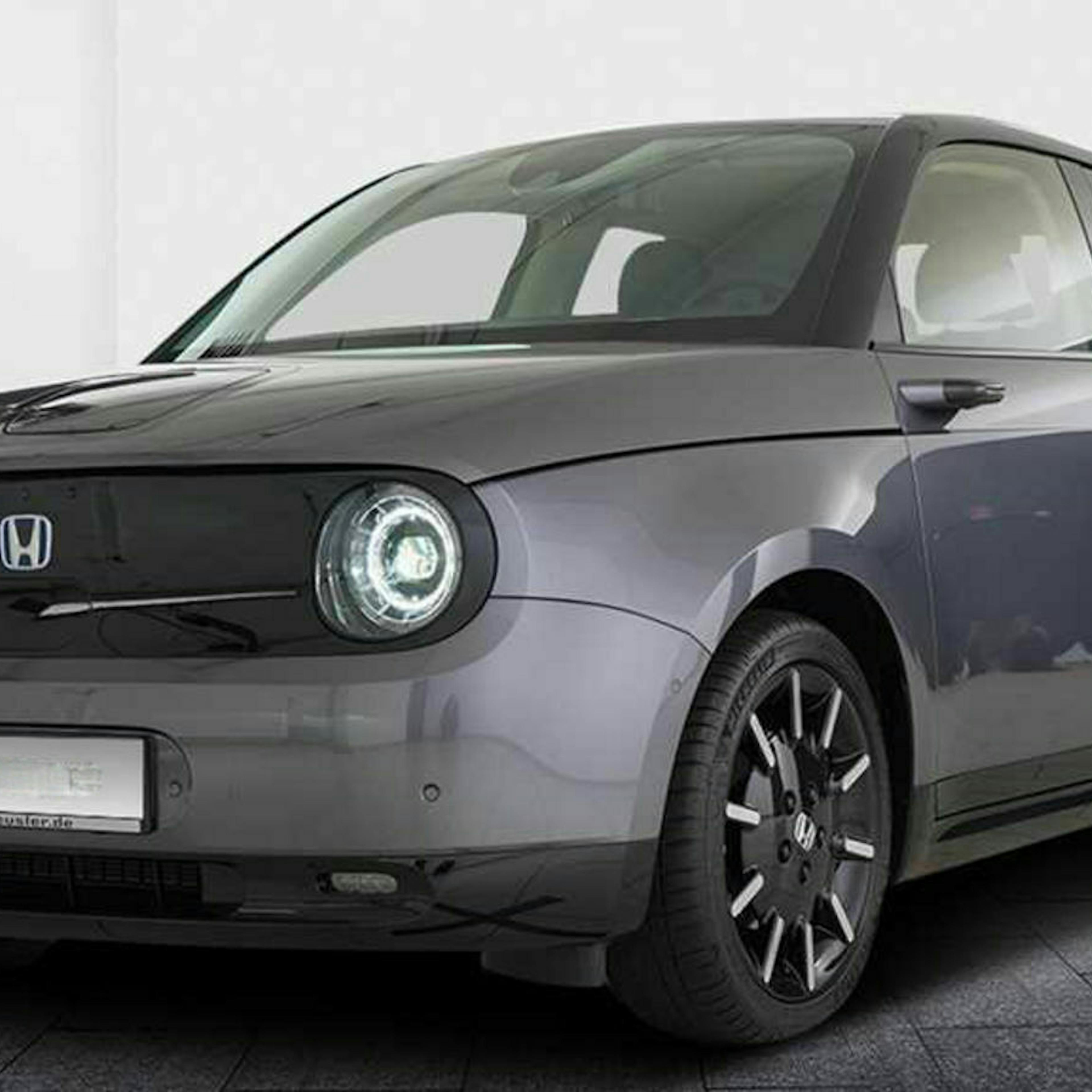 Ein dunkelgrauer Honda E steht vor einer weißen Wand.