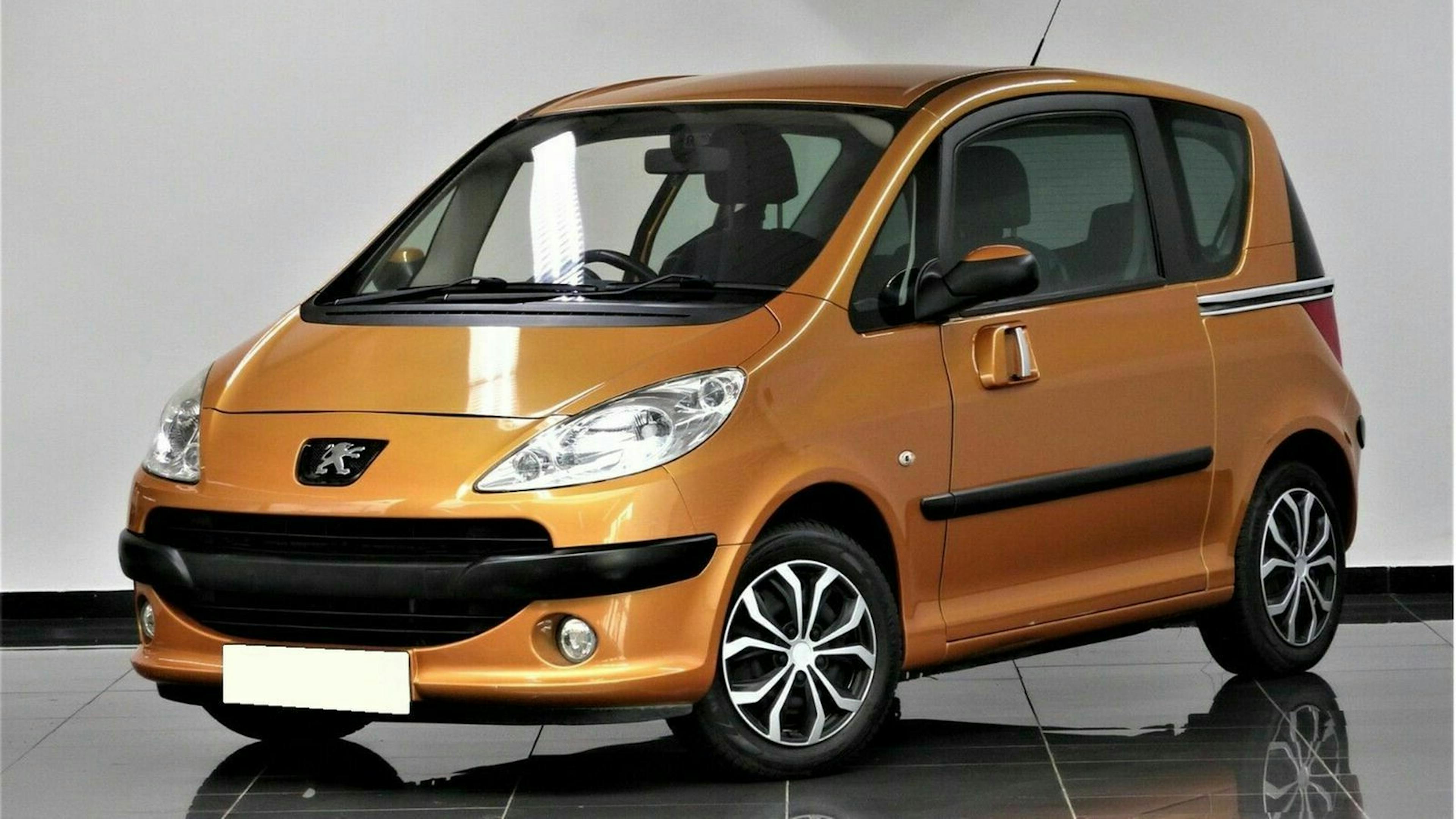 Kompakter, orangefarbener Stadtwagen mit Peugeot-Logo, zweifarbigem Kühlergrill und markanten Felgen auf glänzendem Ausstellungsboden.
