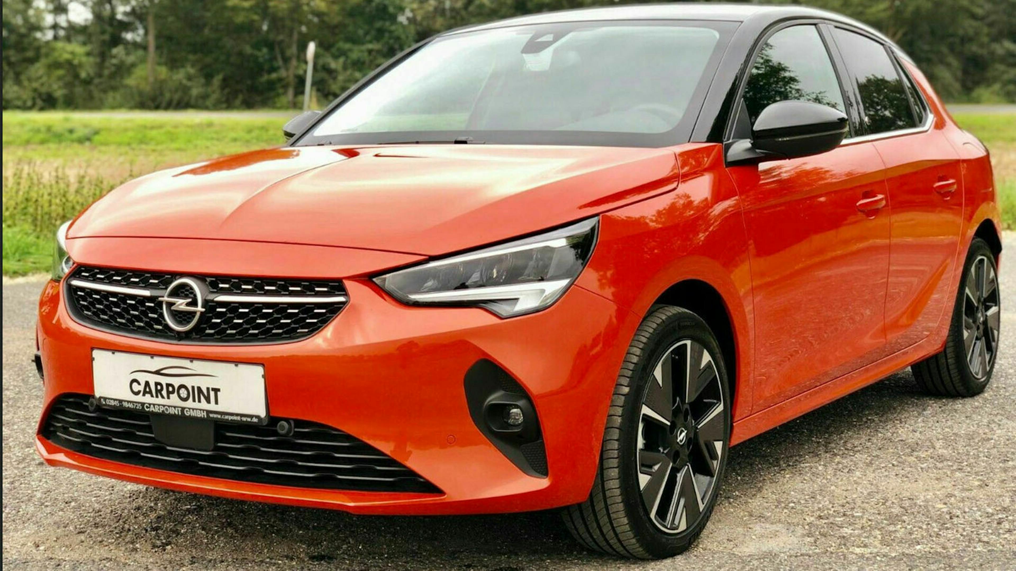 Ein roter Opel e-Corsa steht auf einem Parkplatz am Waldrand