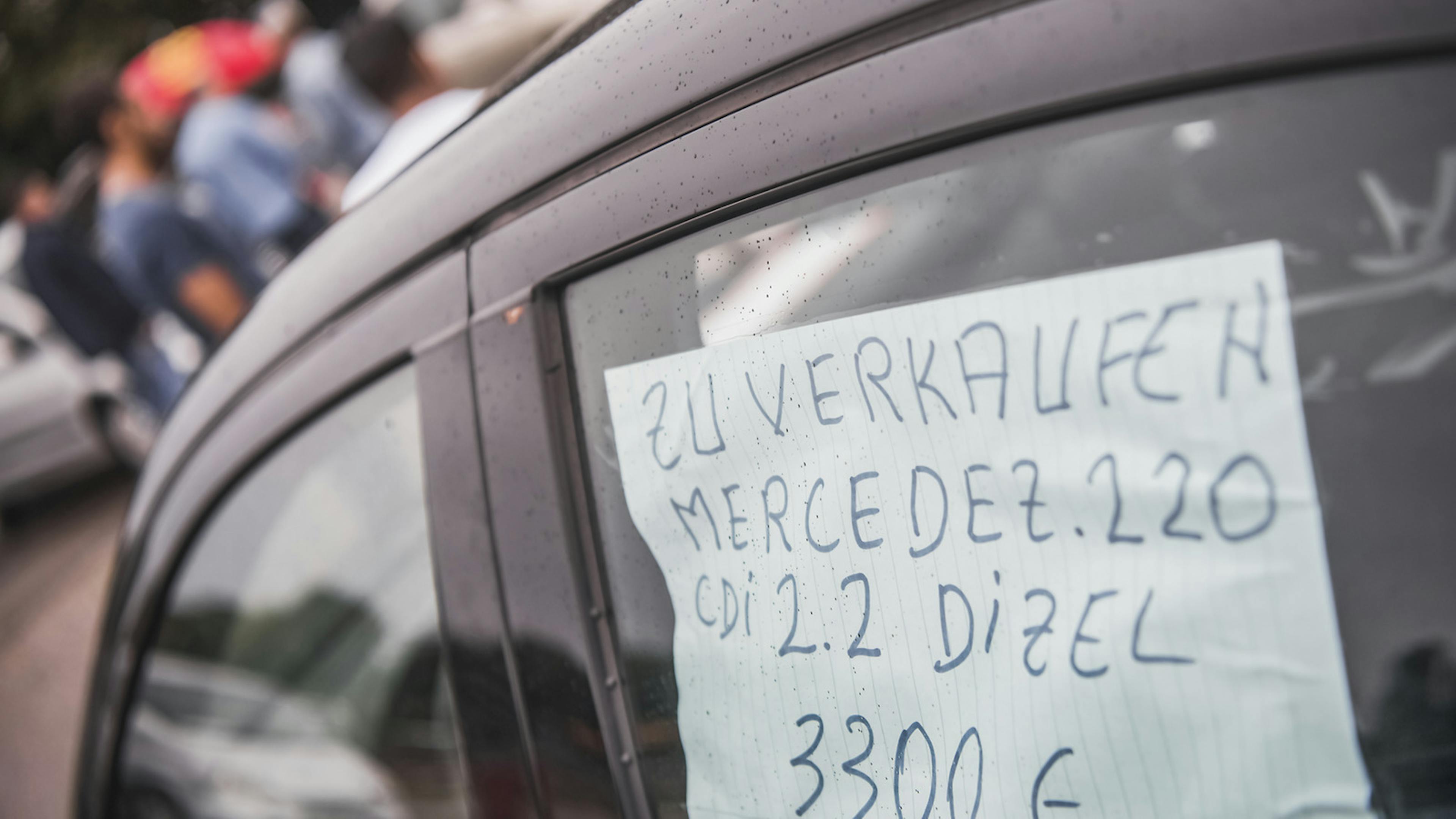 Ein handgeschriebener Zettel mit einer Verkaufsanzeige hängt im Fenster eines Autos
