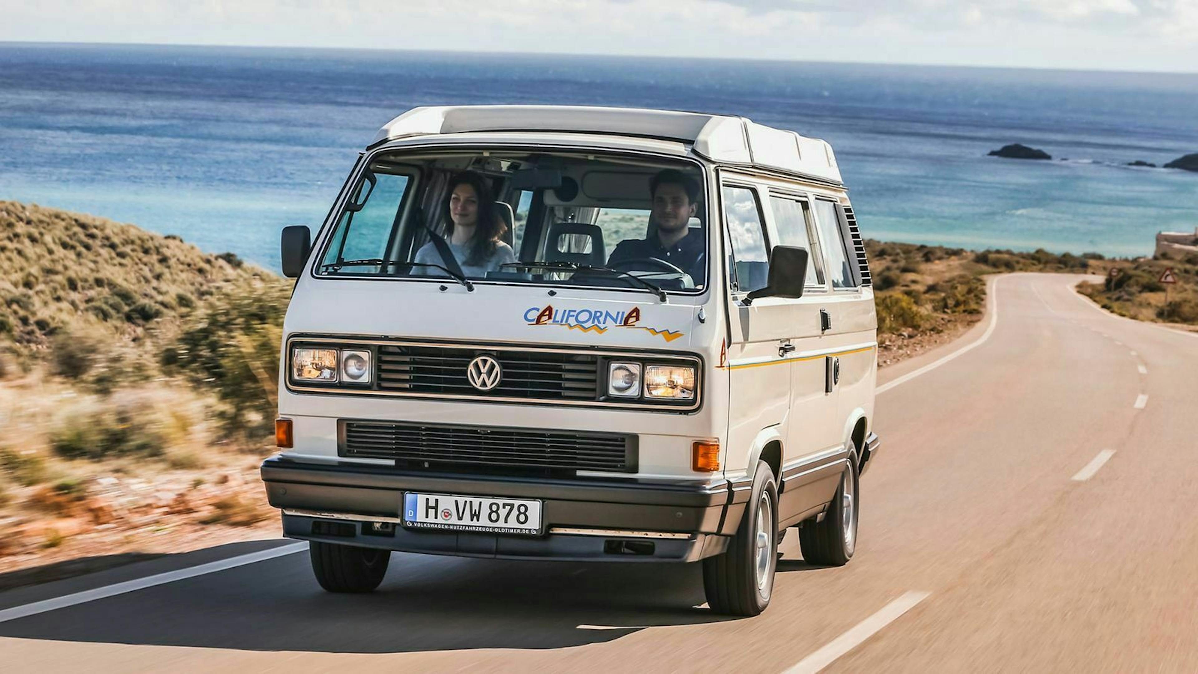 Ein weißer VW T3 California fährt eine Küstenstraße entlang
