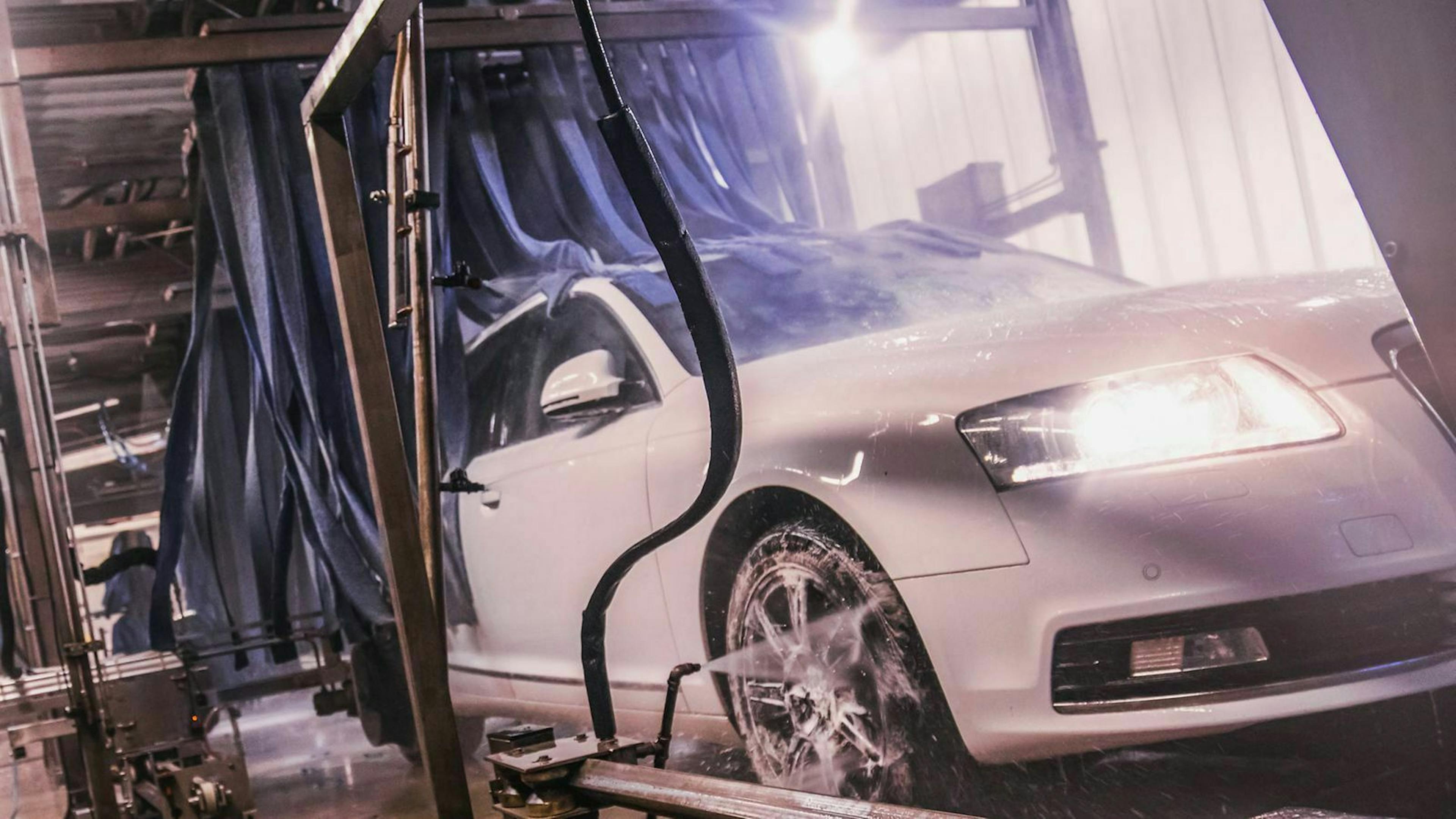 Ein silbergrauer Audi A6 wird durch eine Autowaschanlage gezogen. 