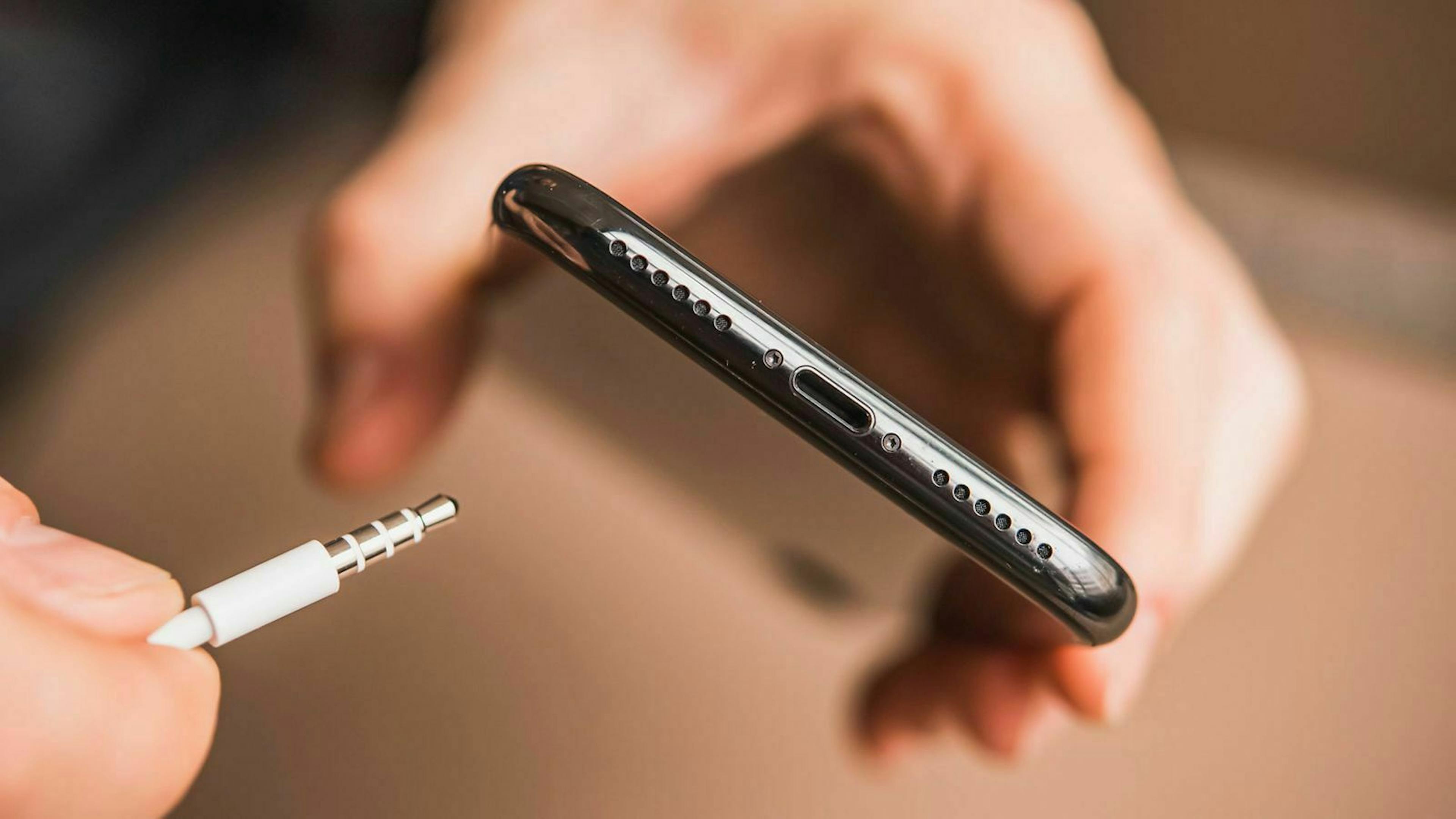Jemand hält einen Klinkenstecker an ein Smartphone, das über keine passende Buchse verfügt.