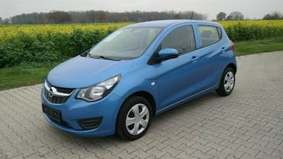 Ein blauer Opel Karl steht auf einem Parkplatz vor einem Rapsfeld