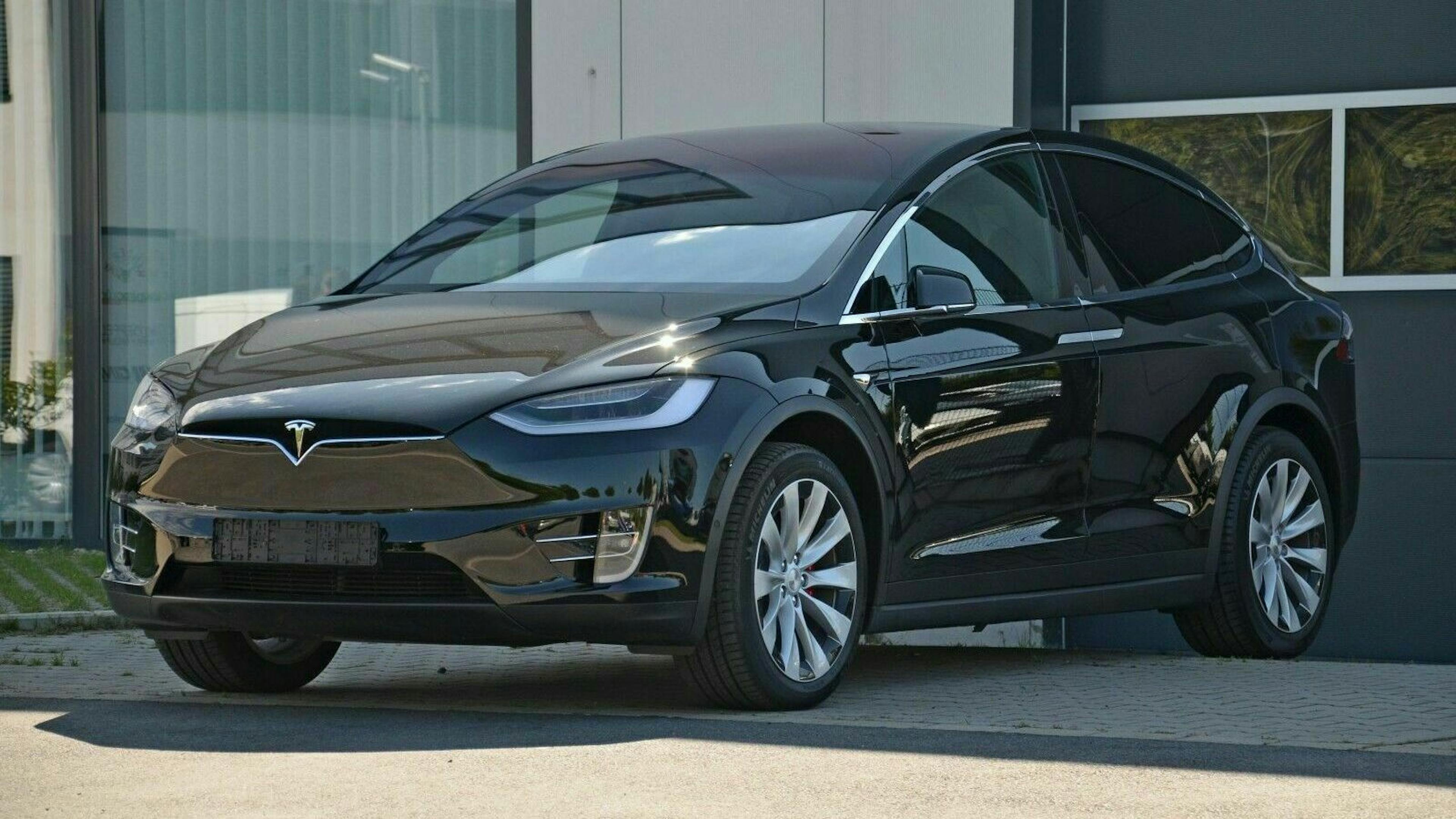 Schwarzes Elektroauto, Modell SUV, geparkt vor einem modernen Gebäude. Elegante Linien, glänzende Lackierung, große Felgen.