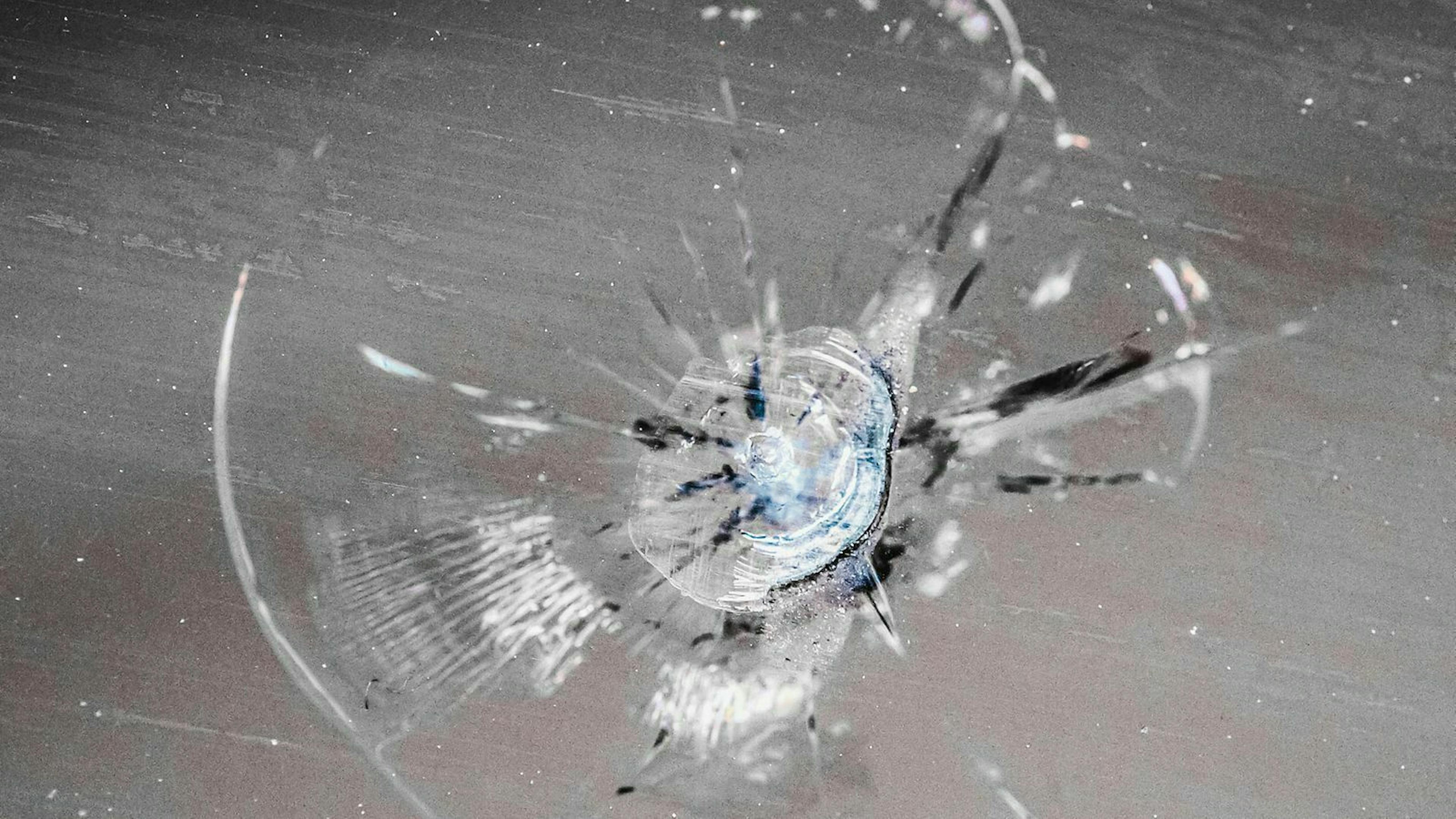 Ein Steinschlag in Nahaufnahme: Von einem zentralen Einschlagspunkt ziehen sich Haarrisse sternförmig in die Glasfläche.