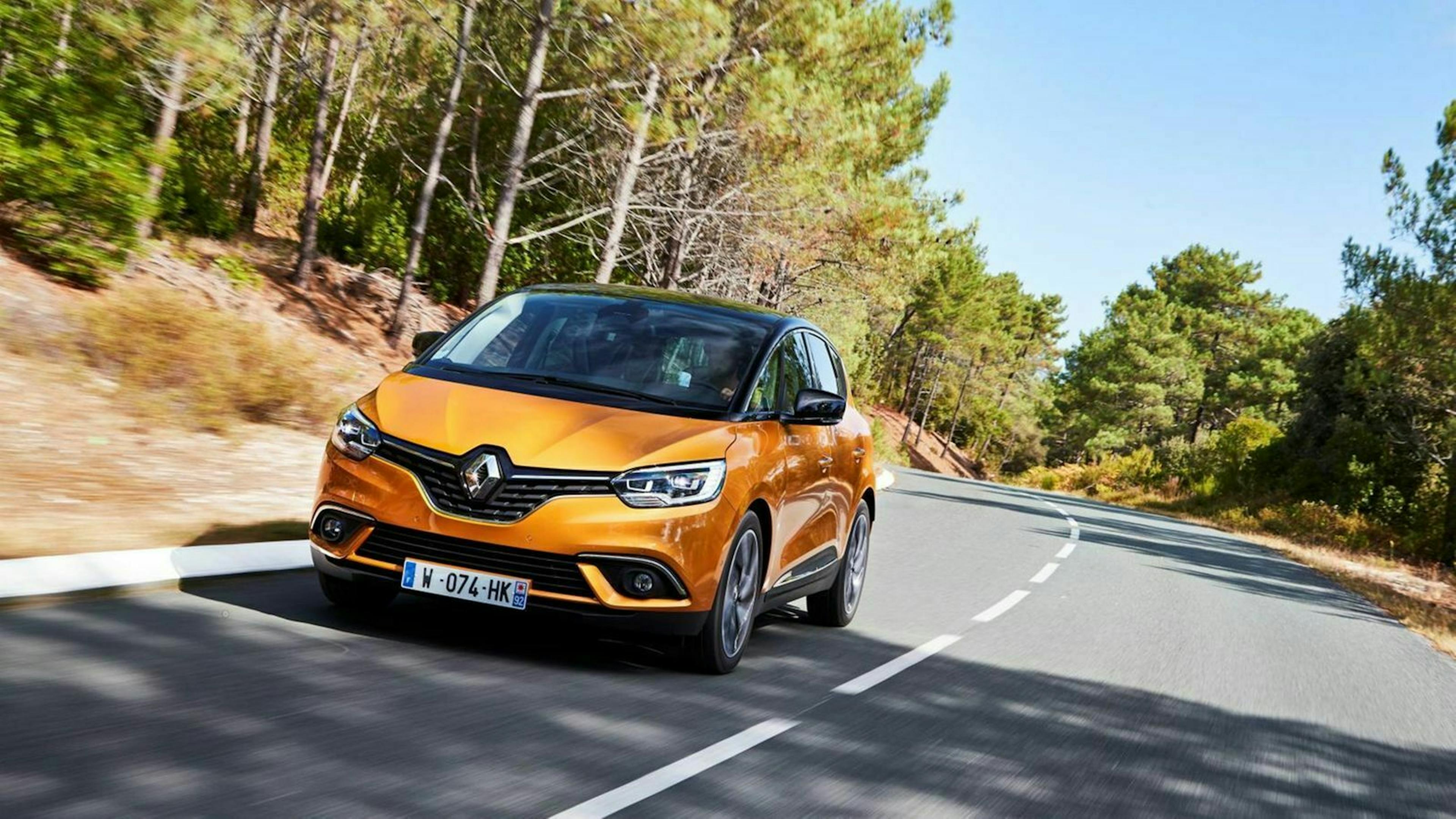 Ein orangefarbener Renault Scenic fährt eine Landstraße entlang