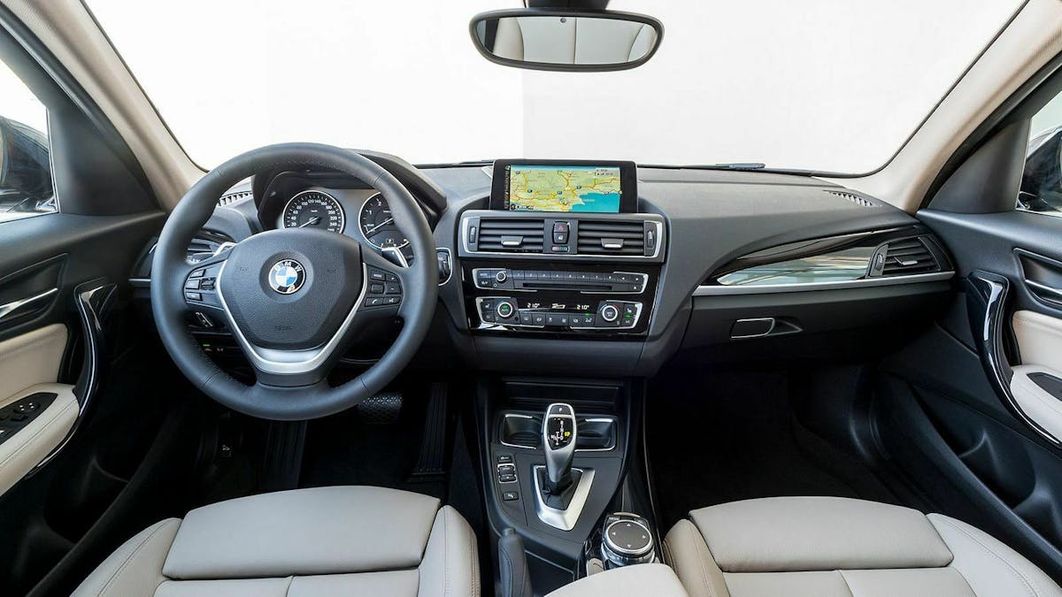 Zu sehen ist das Cockpit des BMW 120 xDrive 5dr. Die Polsterung ist beige und das Amaturenbrett schwarz mit silbernen Akzenten