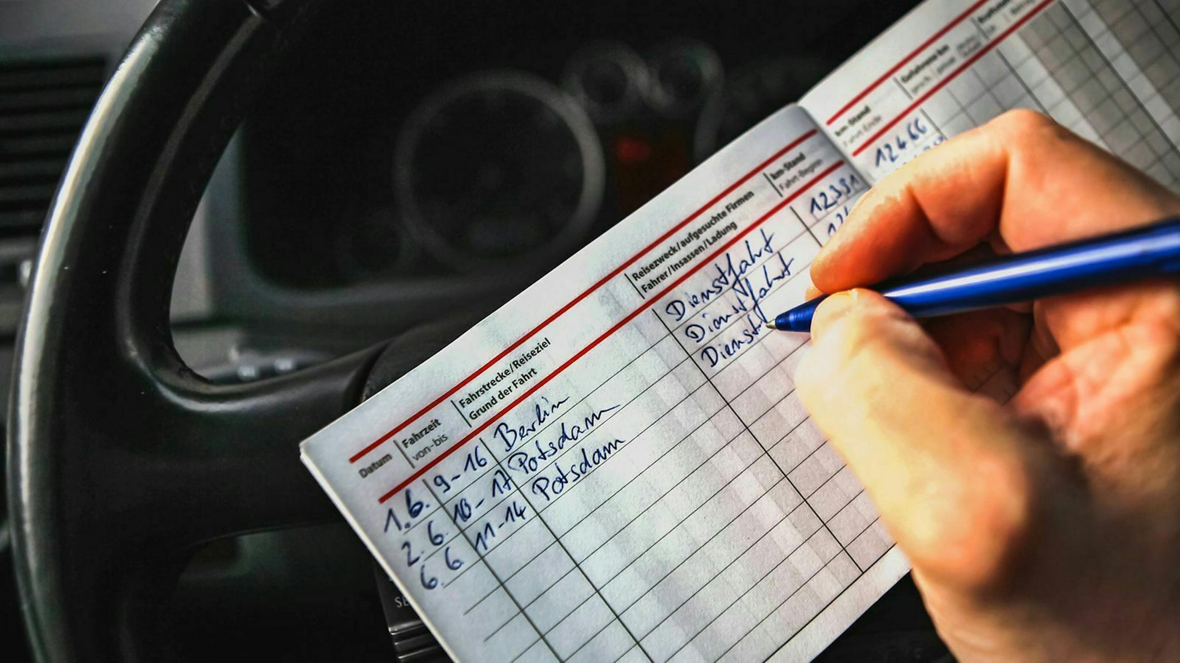 Jemand sitzt am Steuer seines Dienstwagens und füllt ein Fahrtenbuch aus.