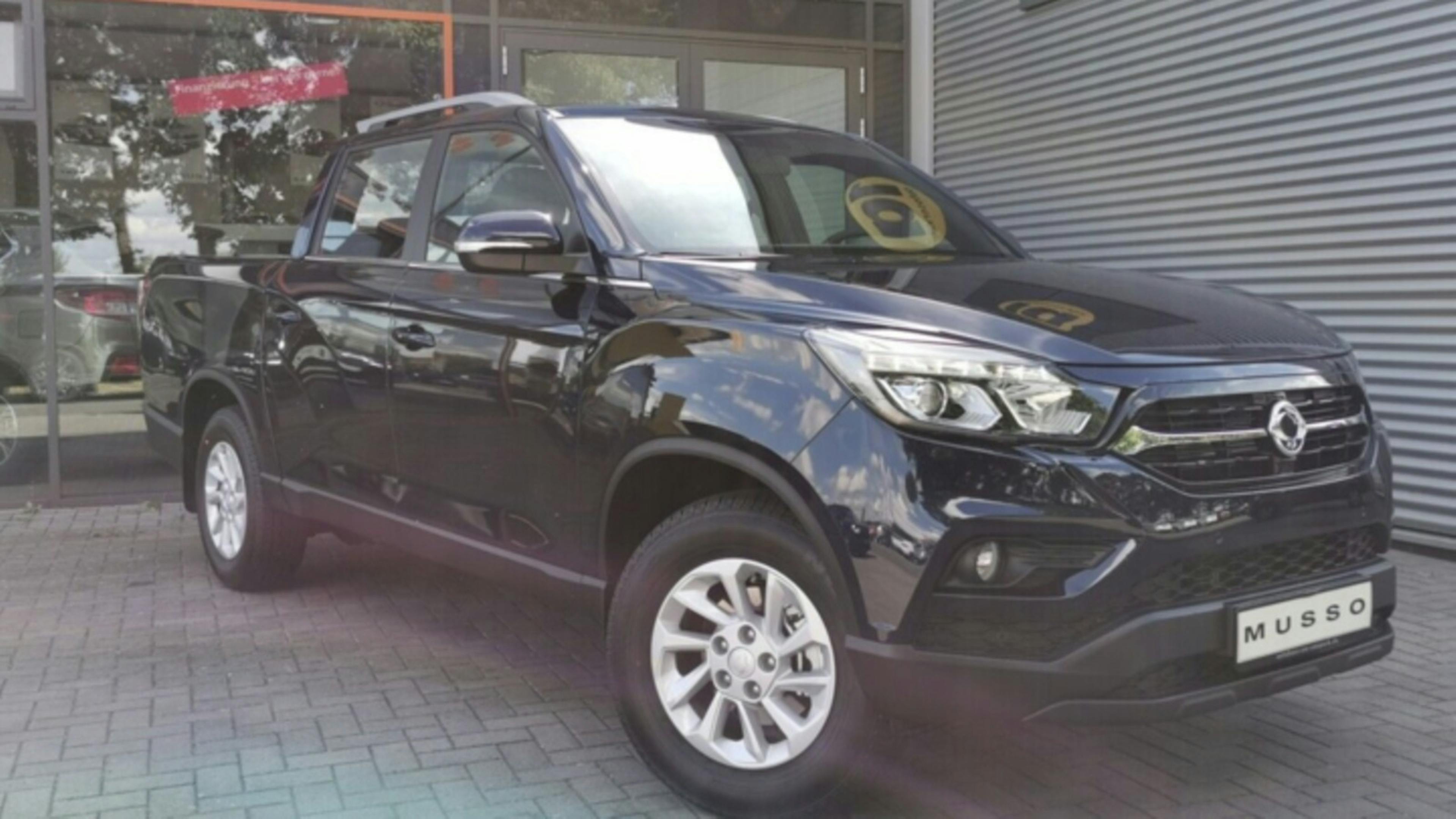 Ein schwarzer SsangYong Musso Pick-up steht vor einem grauen Rolltor.