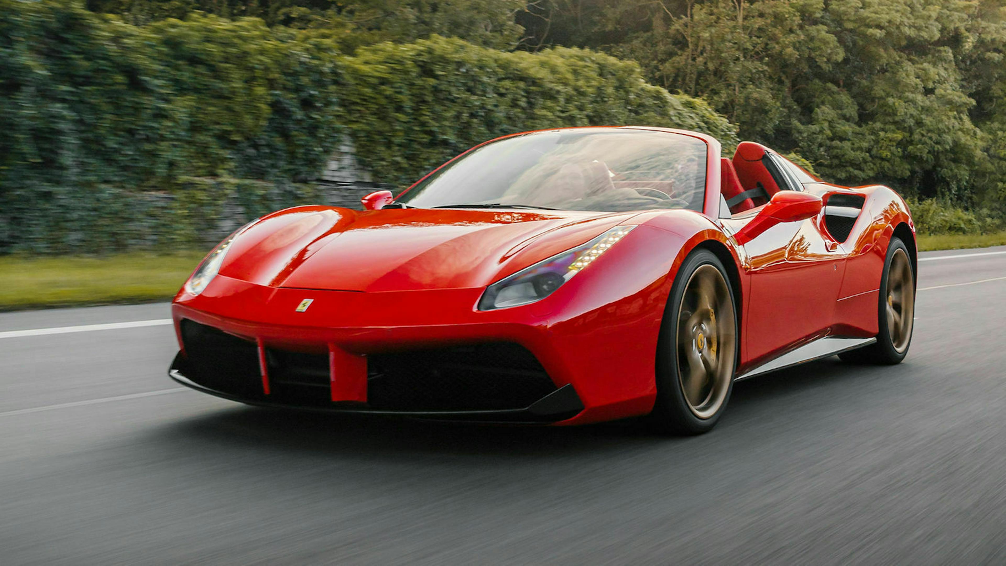 Ein roter PKW der Marke Ferrari fährt eine Landstrasse entlang