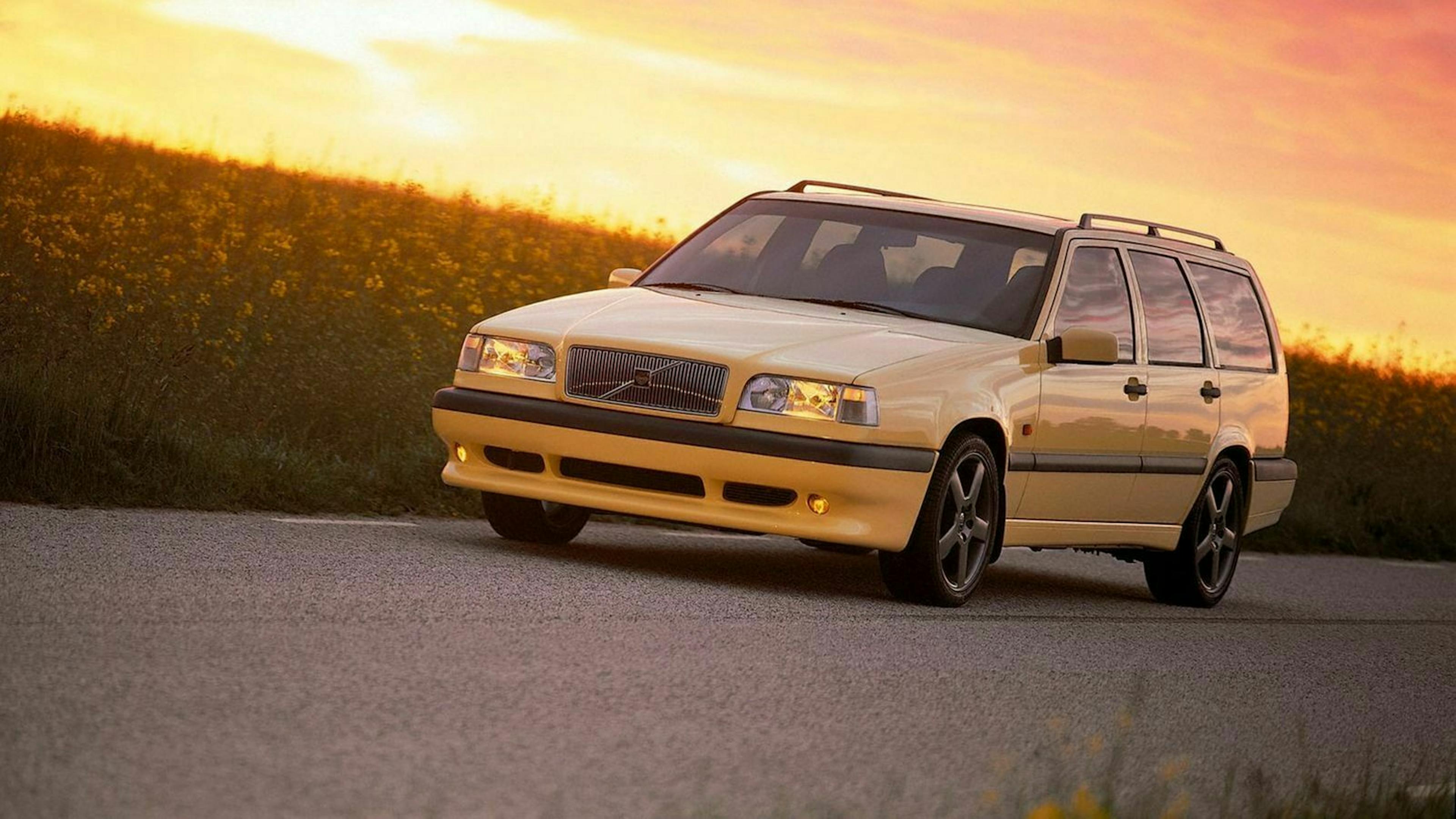 Ein gelber Volvo 850 Oldtimer fährt im Sonnenuntergang eine Landstraße entlang.
