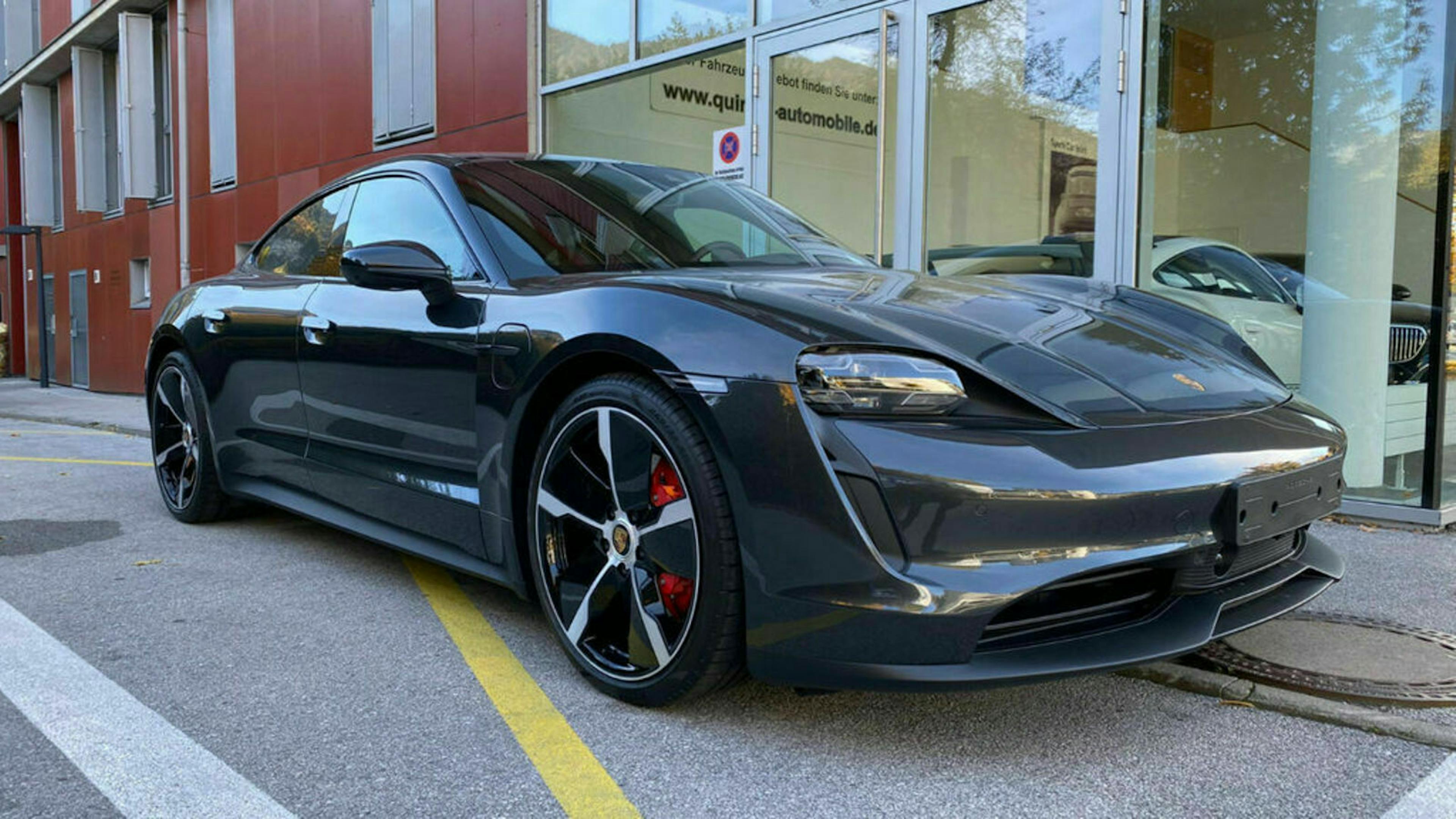 Ein schwarzer Porsche Taycan 4S steht auf vor einem Gebäude mit Glasfront 