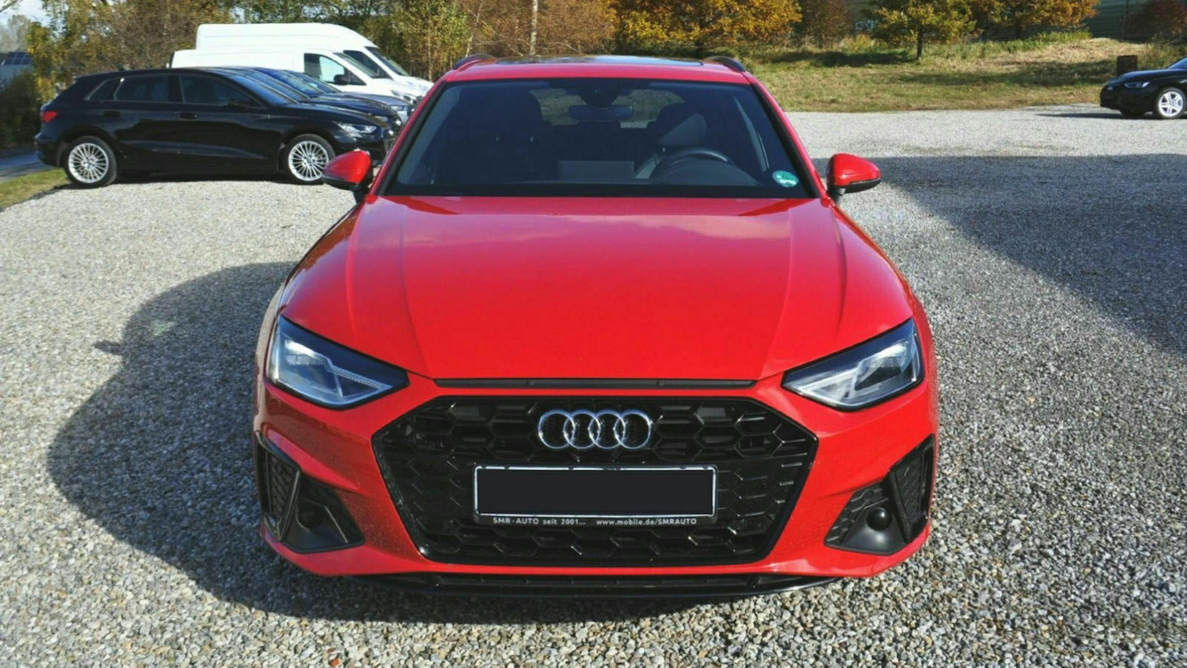 Ein roter Audi A4 steht auf einem Parkplatz, im Hintergrund sind ein weißer Van und ein schwarzer PKW zu sehen