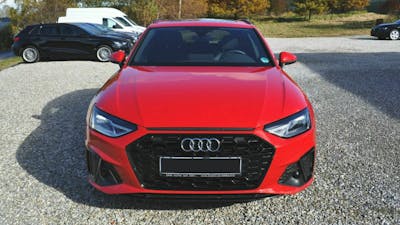 Ein roter Audi A4 steht auf einem Parkplatz, im Hintergrund sind ein weißer Van und ein schwarzer PKW zu sehen