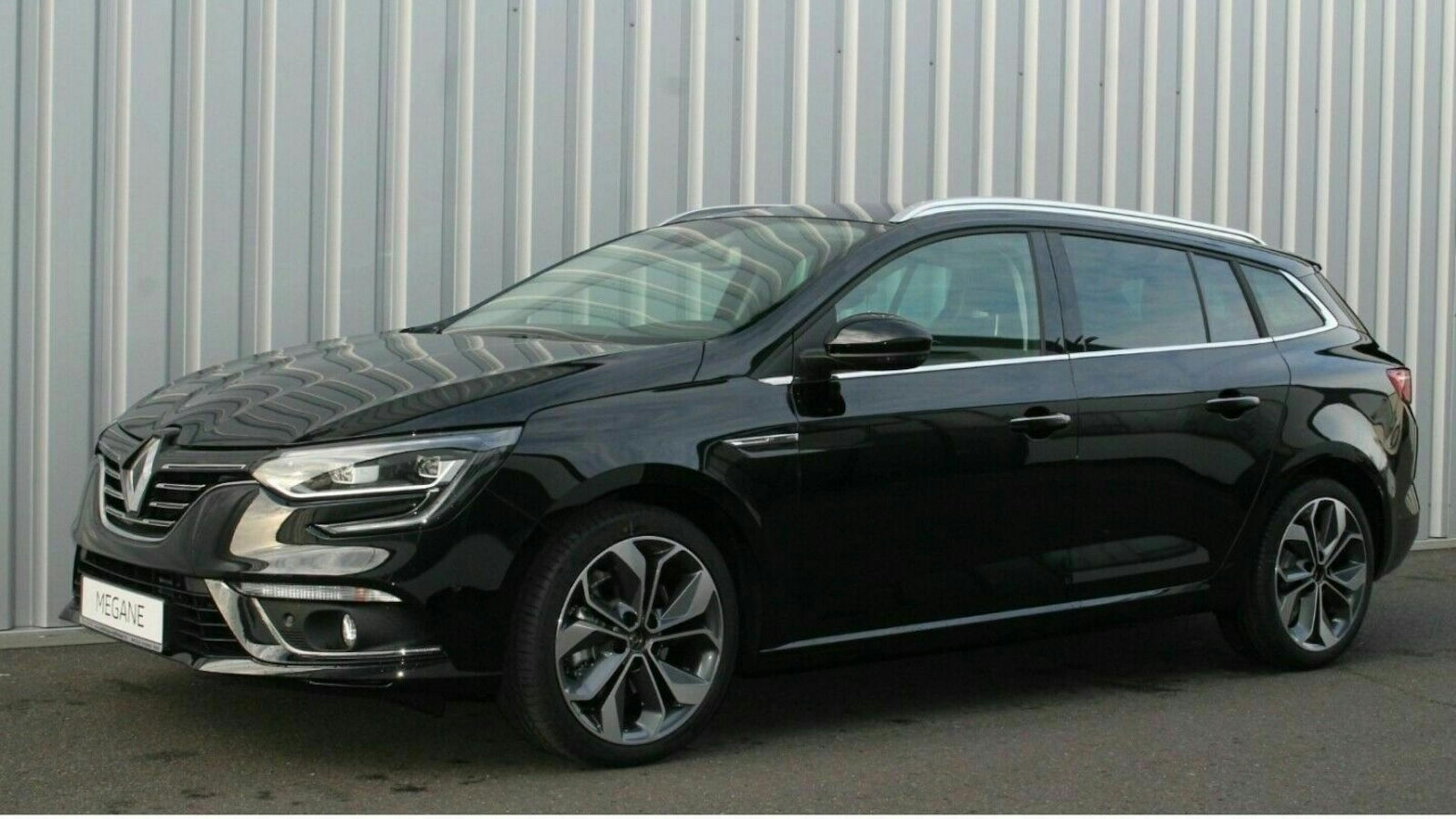 Schwarzer Renault Kombi vor einer grauen Industriehallenwand, schräg von vorne fotografiert.