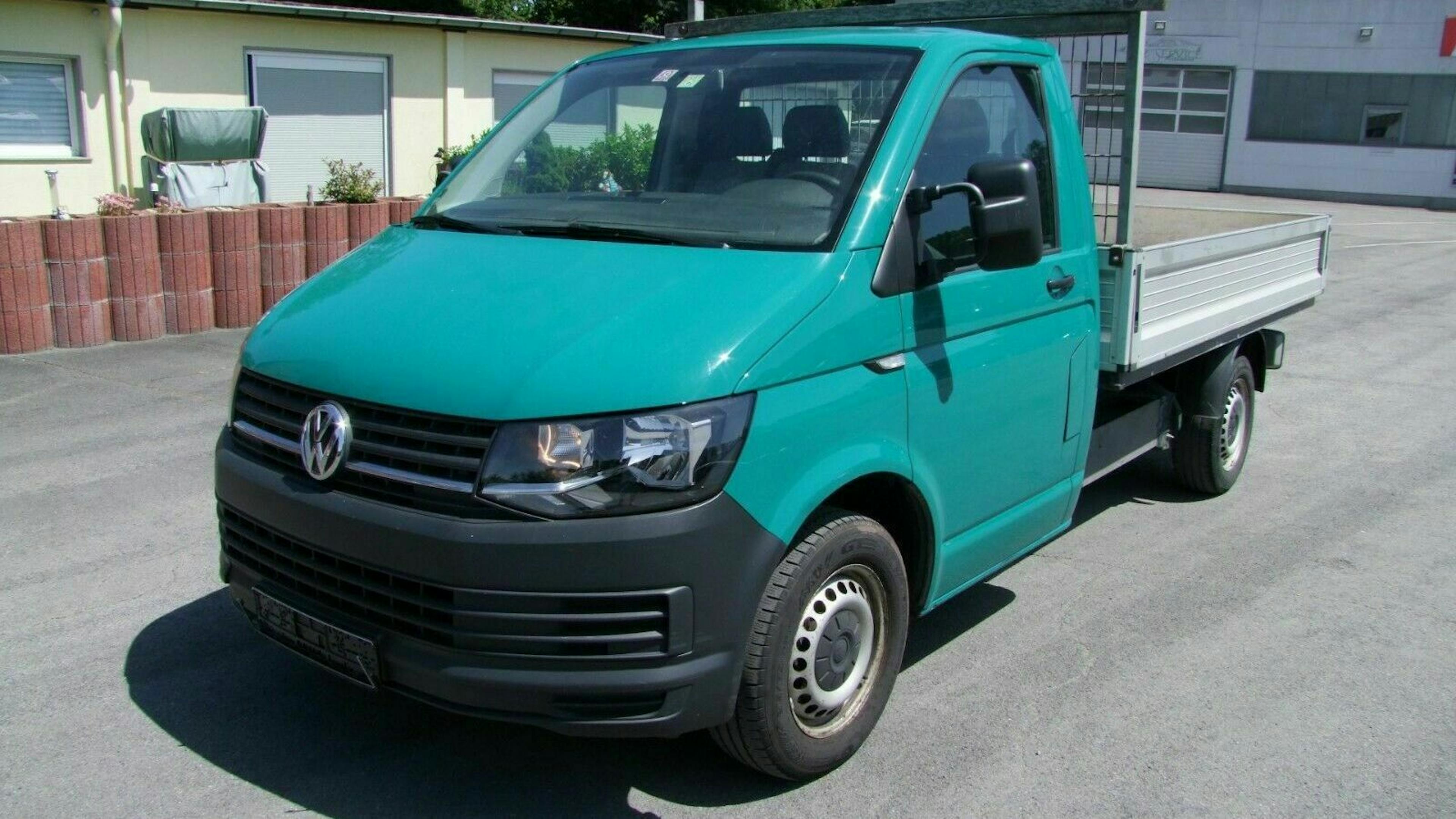 Ein türkisfarbener VW T6 Pritschenwagen steht vor einem hellen Haus.