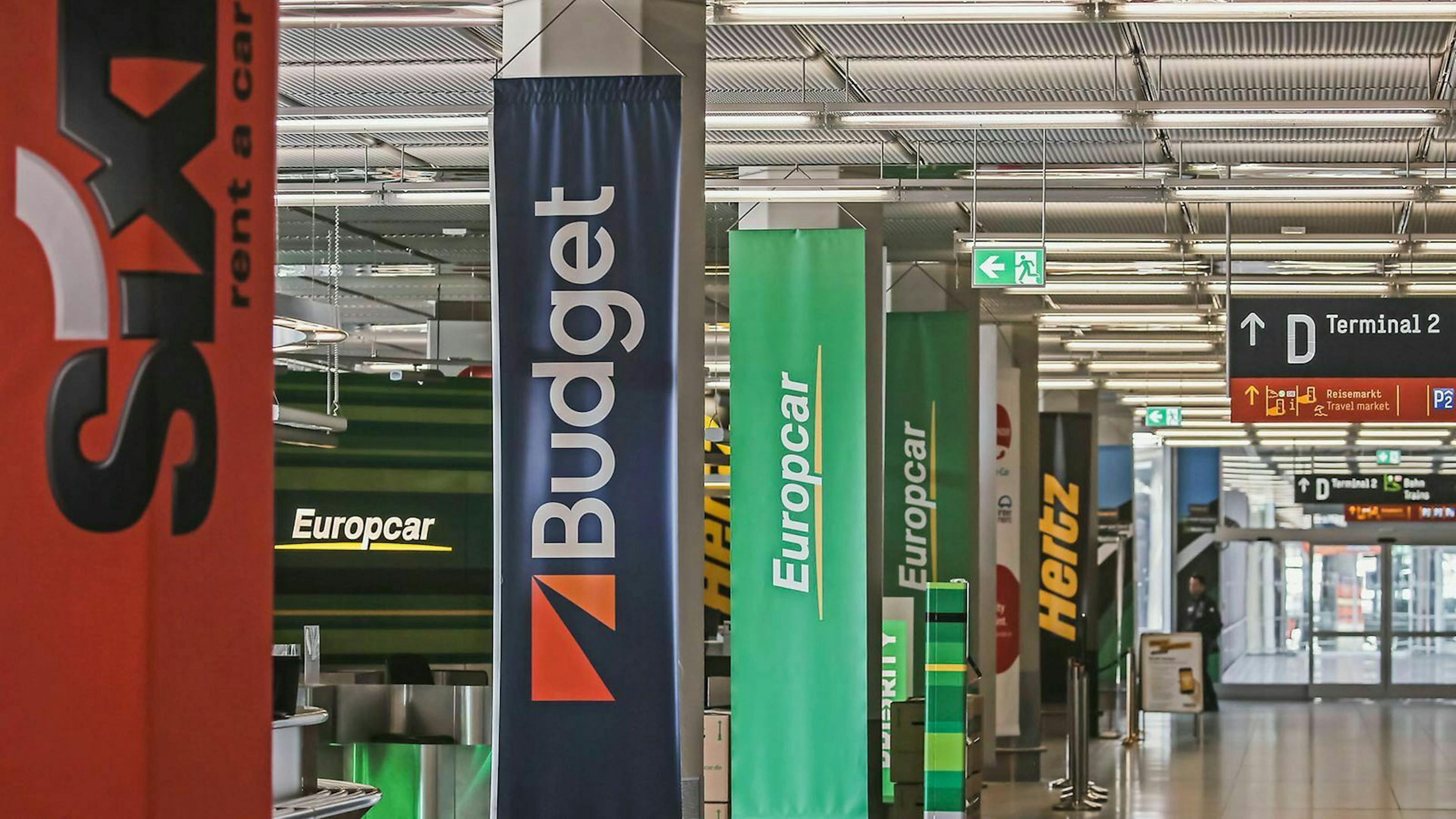 An einem Flughfafen sind Banner verschiedener Autovermietungen der Reihe nach von der Decke abgehängt.