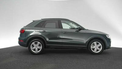 Ein dunkelgrauer Audi Q3 steht vor einer weißen Wand