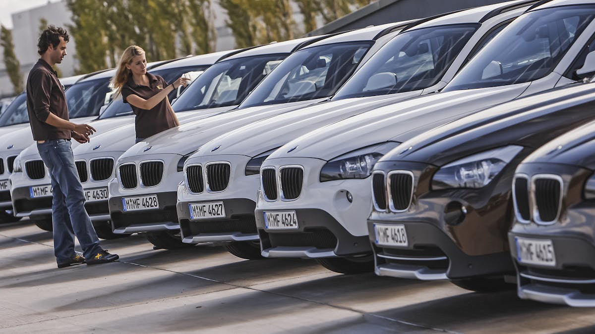 Zwei Personen begutachten ein Fahrzeug, das in einer Reihe mit SUVs gleicher Bauart geparkt steht