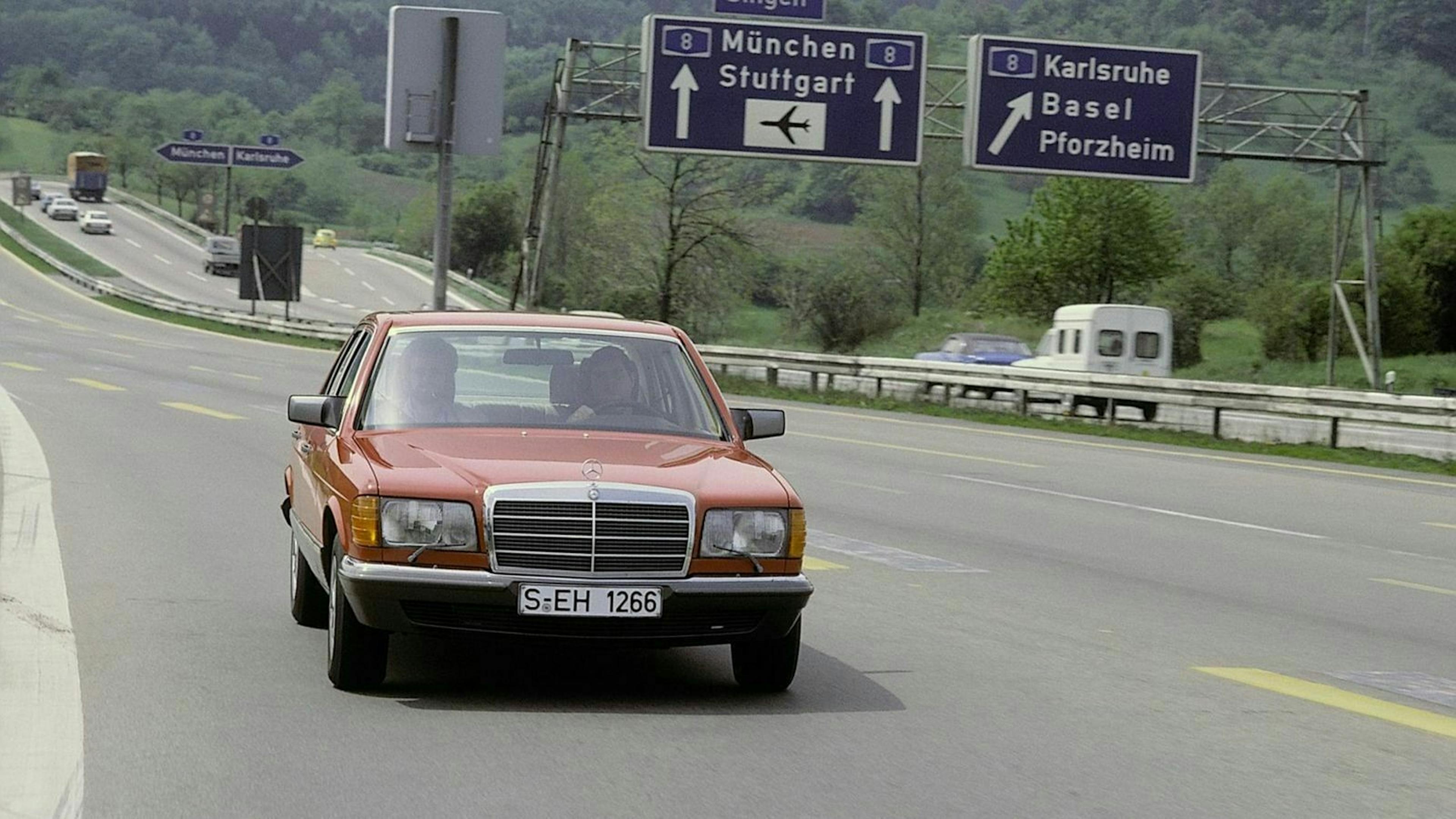Ein roter Mercedes-Benz fährt auf einer Autobahn, im Hintergrund Verkehrszeichen mit Richtungen nach München, Stuttgart und Karlsruhe.