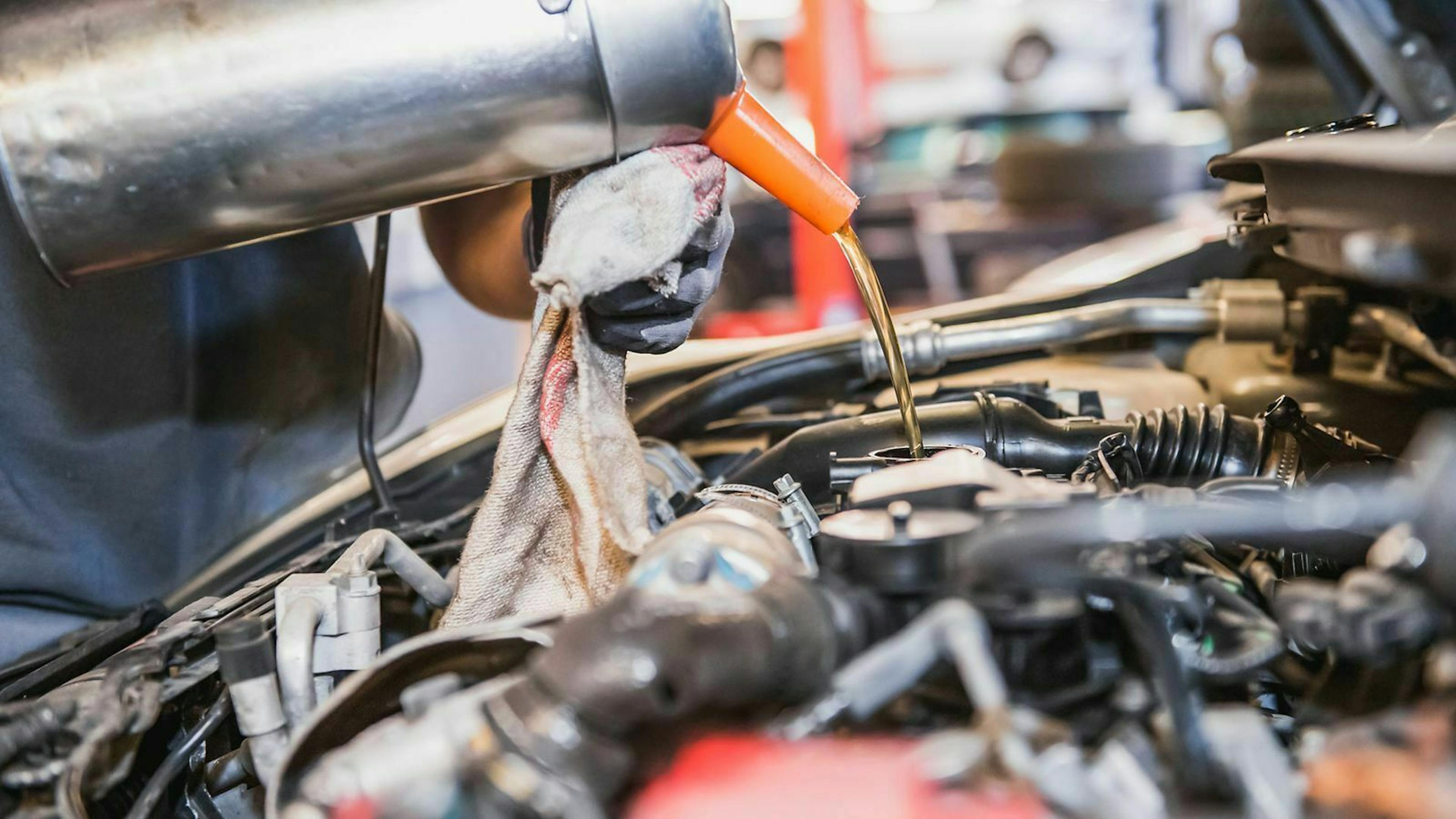 Jemand füllt mit einer Aluklanne Öl in den Motor eines Autos.