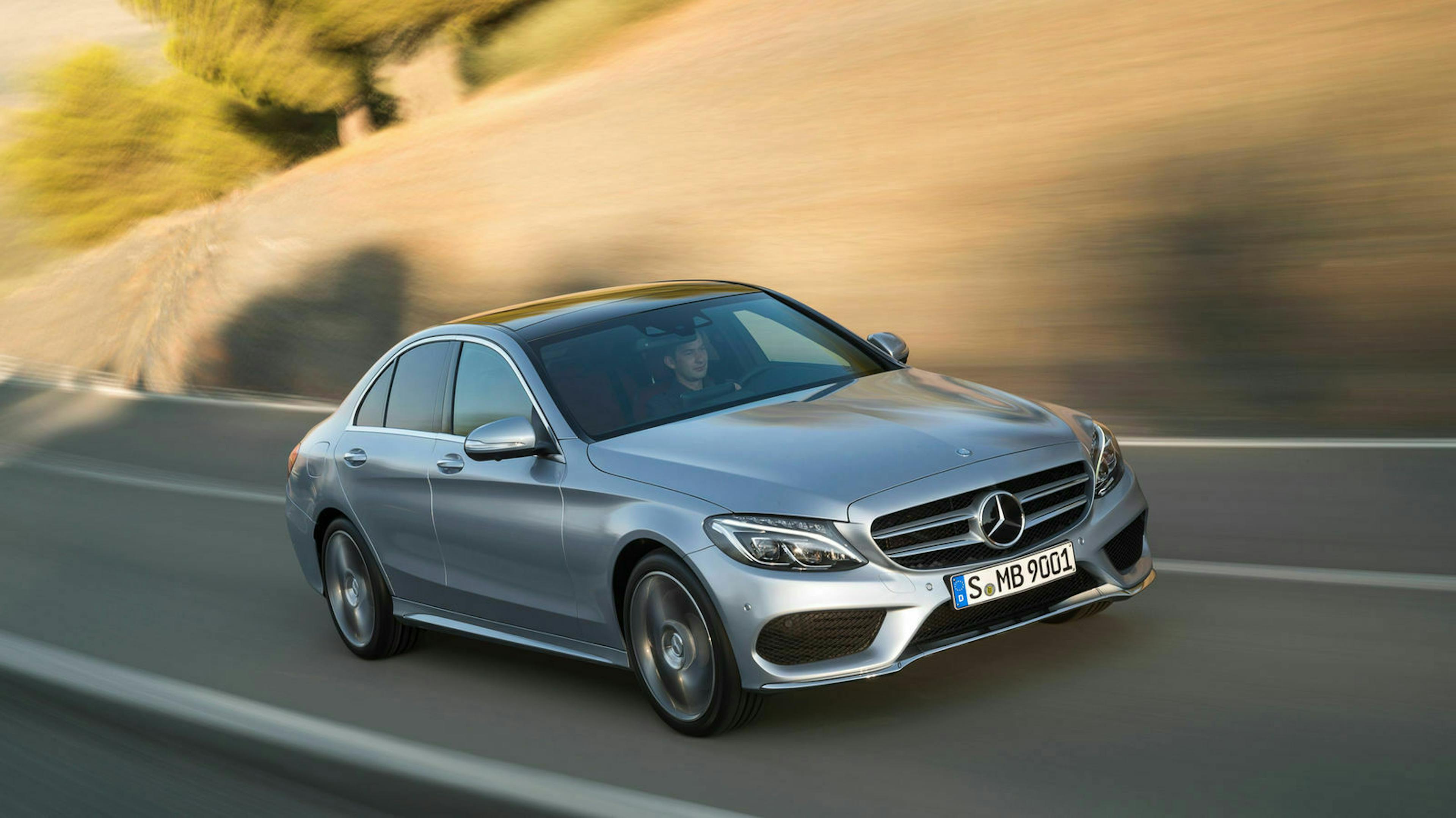 Eine dunkelgraue Mercedes-Benz C-Klasse mit Heckantrieb fährt eine Straße entlang