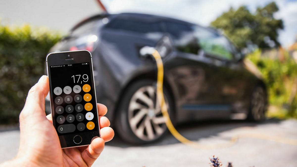 Jemand hält sein Smartphone vor ein Elektroauto. Auf dem Smartphone ist die Taschenrechner-App geöffnet