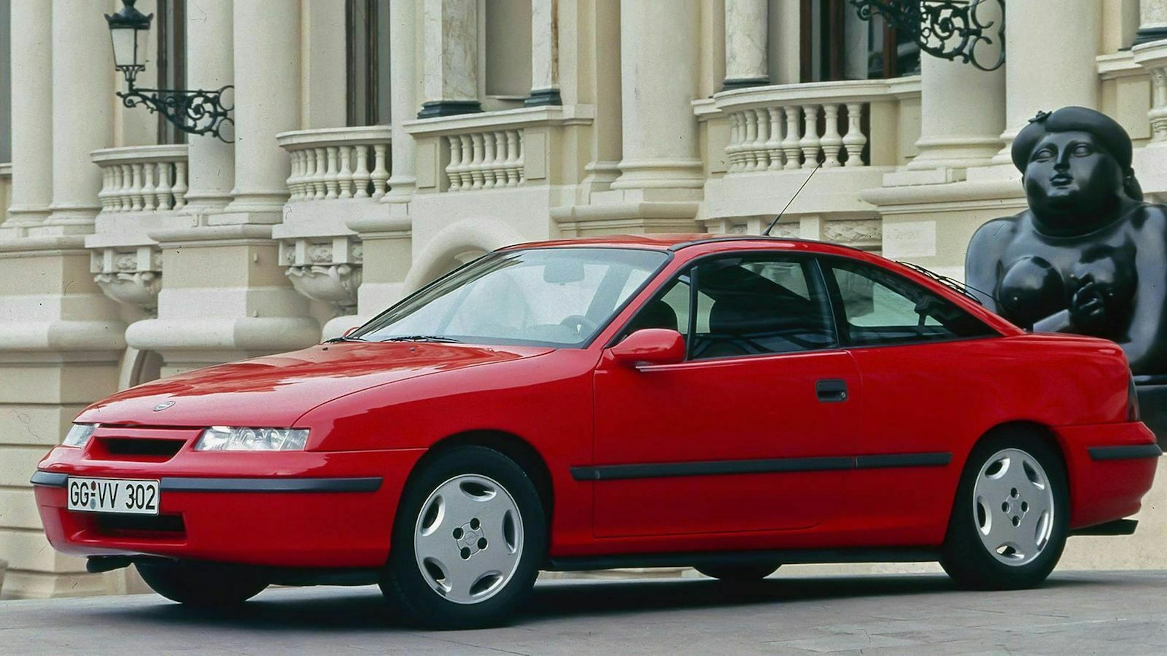 Ein roter Opel Calibra Turbo Oldtimer steht vor einem beigefarbenen Gebäude.