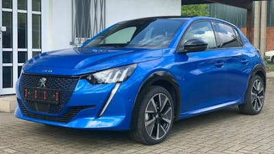 Ein blauer Peugeot e-208 steht vor einem Haus mit weißer Fassade