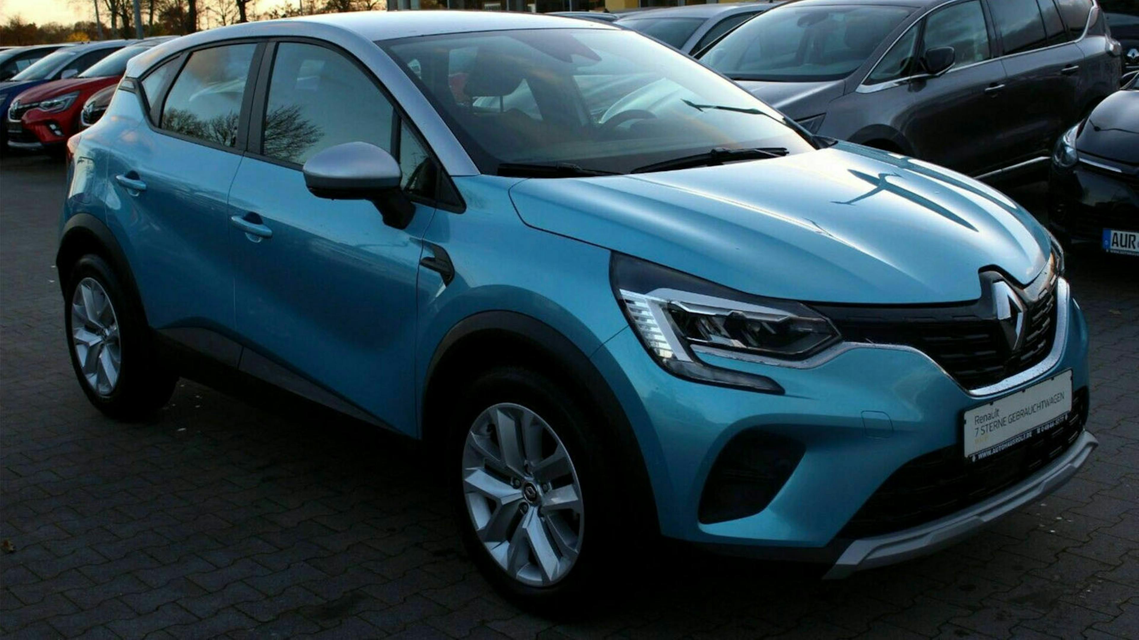Ein türkisfarbener Renault Captur steht auf einem Parkplatz, im Hintergrund sind weitere PKWs zu sehen