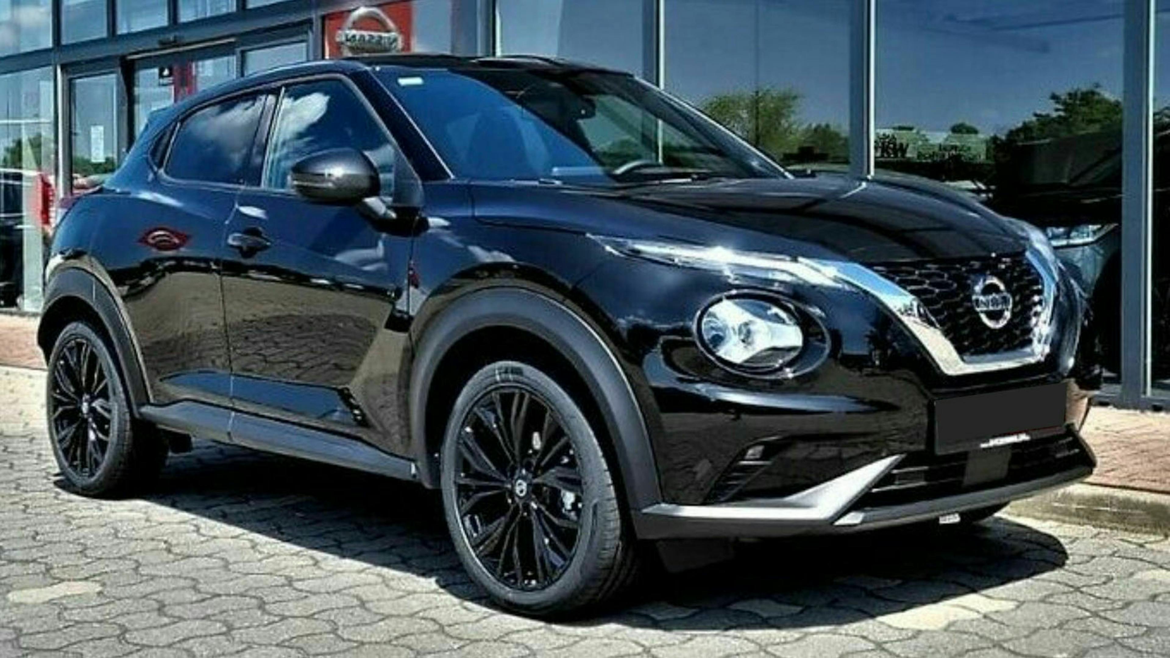 Ein schwarzer Nissan Juke steht auf einem Parkplatz vor einem Gebäude mit Fensterfront
