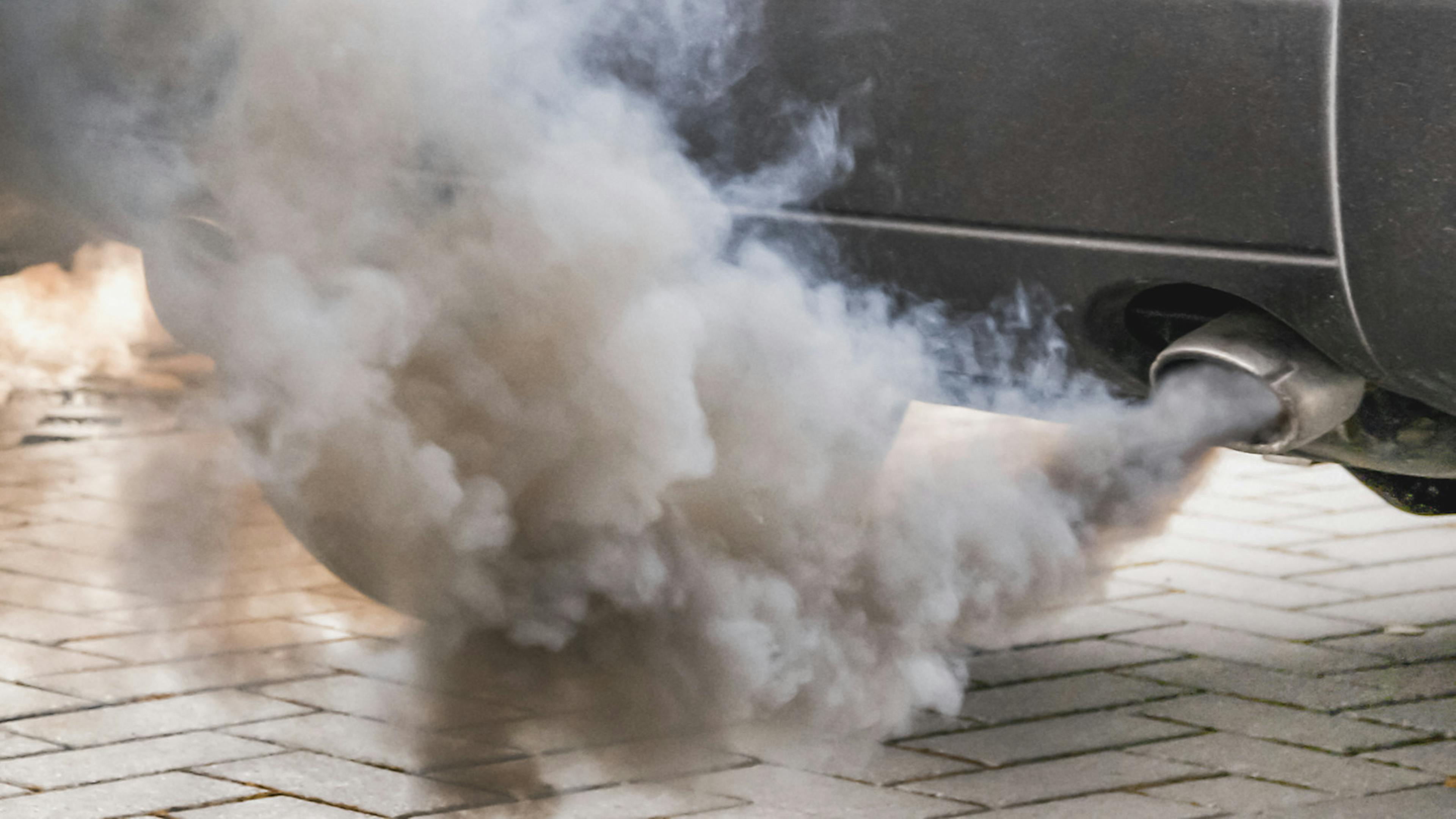 Aus dem Auspuff eines Autos strömt ein dichter Qualm Abgase.