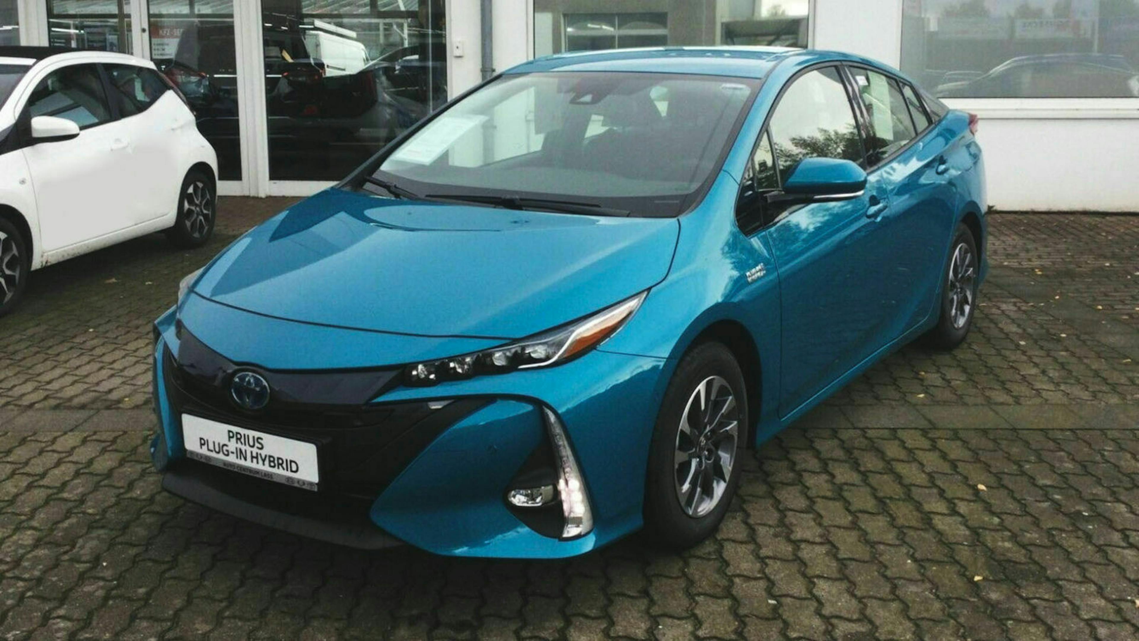 Ein türkiser To​​yota Prius Plug-in steht auf dem Parkplatz eines Autohauses