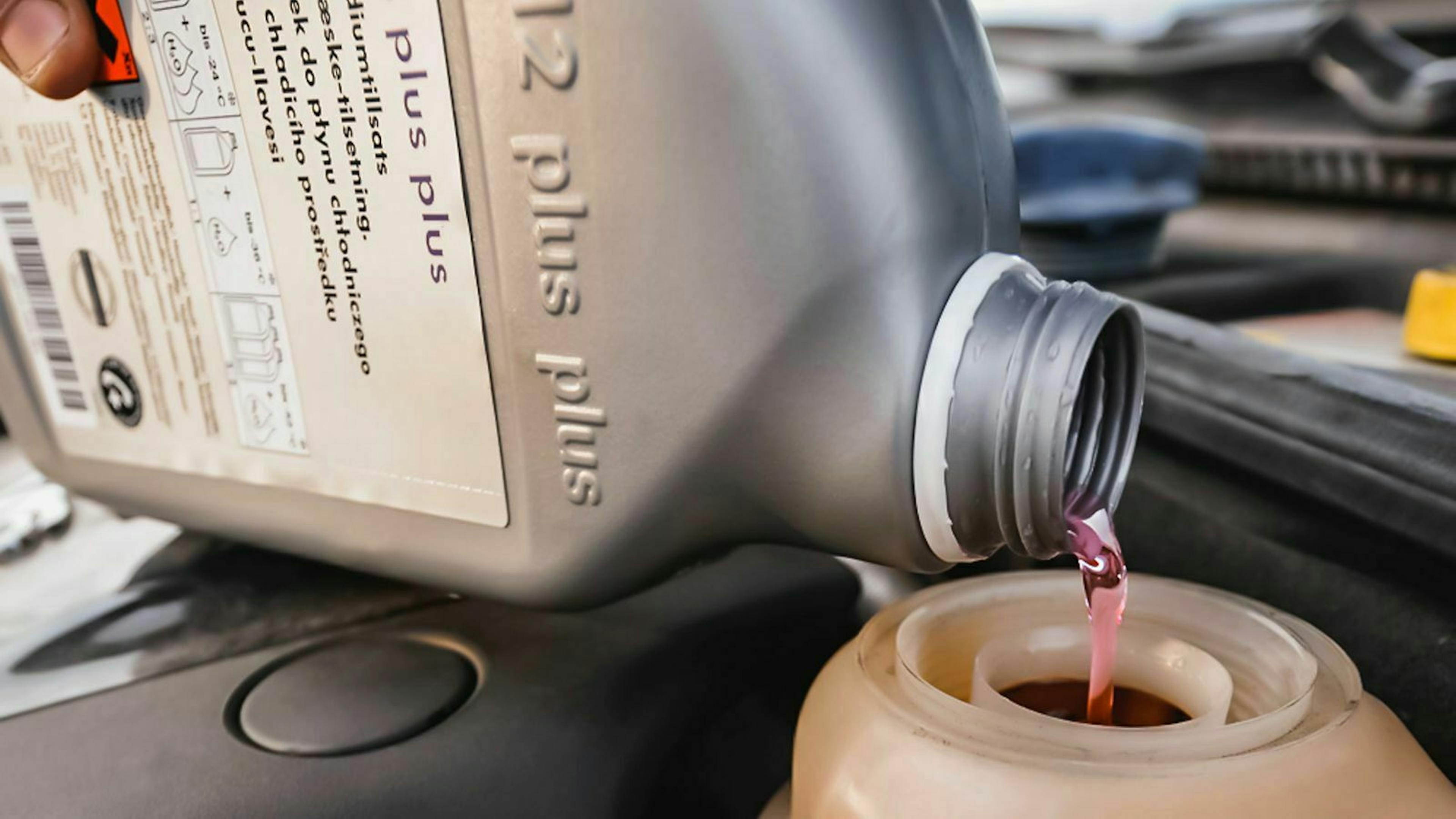 Jemand füllt Frostschutzmittel in den Kühler eines Autos.