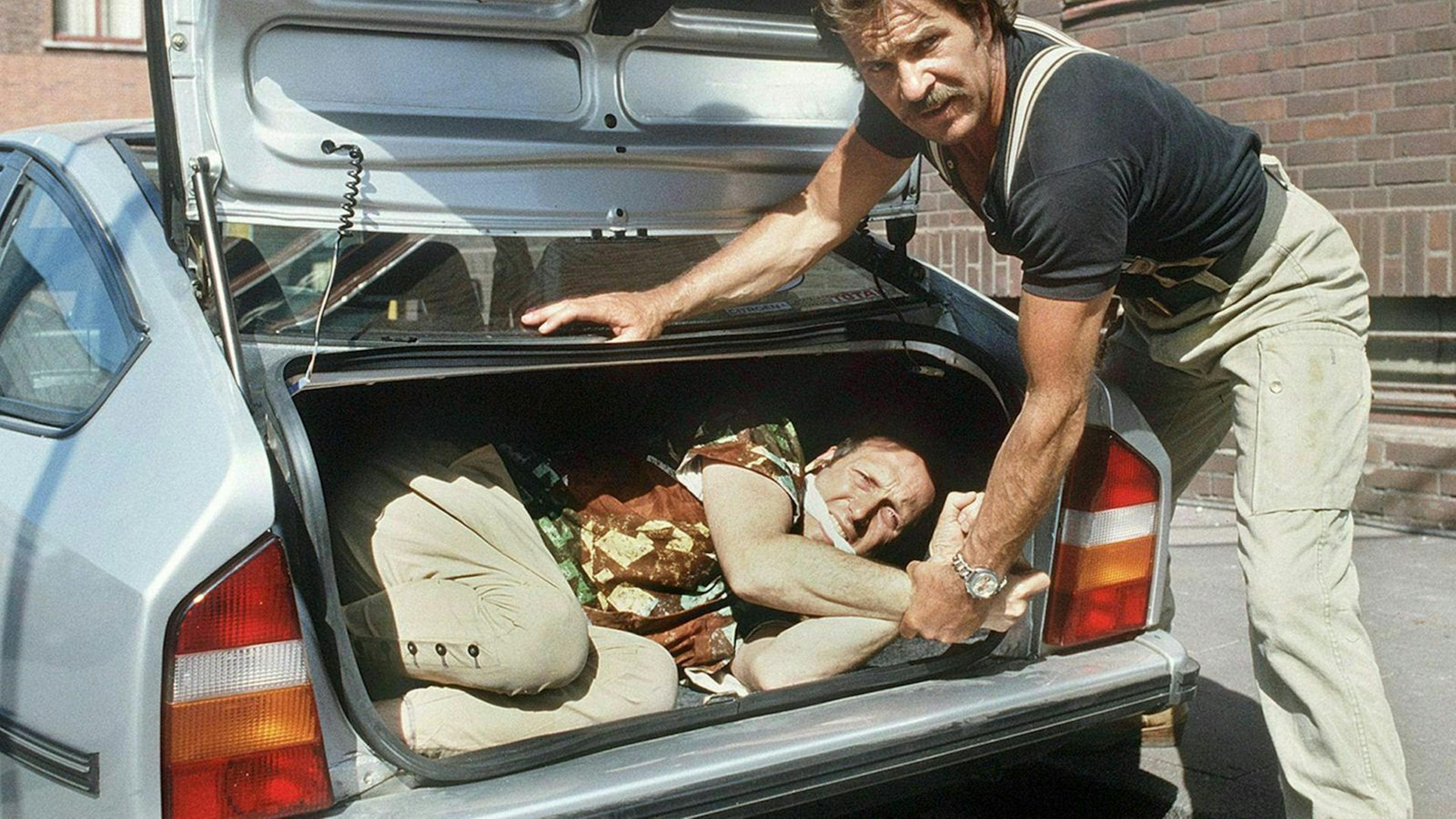 Zu sehen ist ein gefesselter Mann in einem Kofferraum