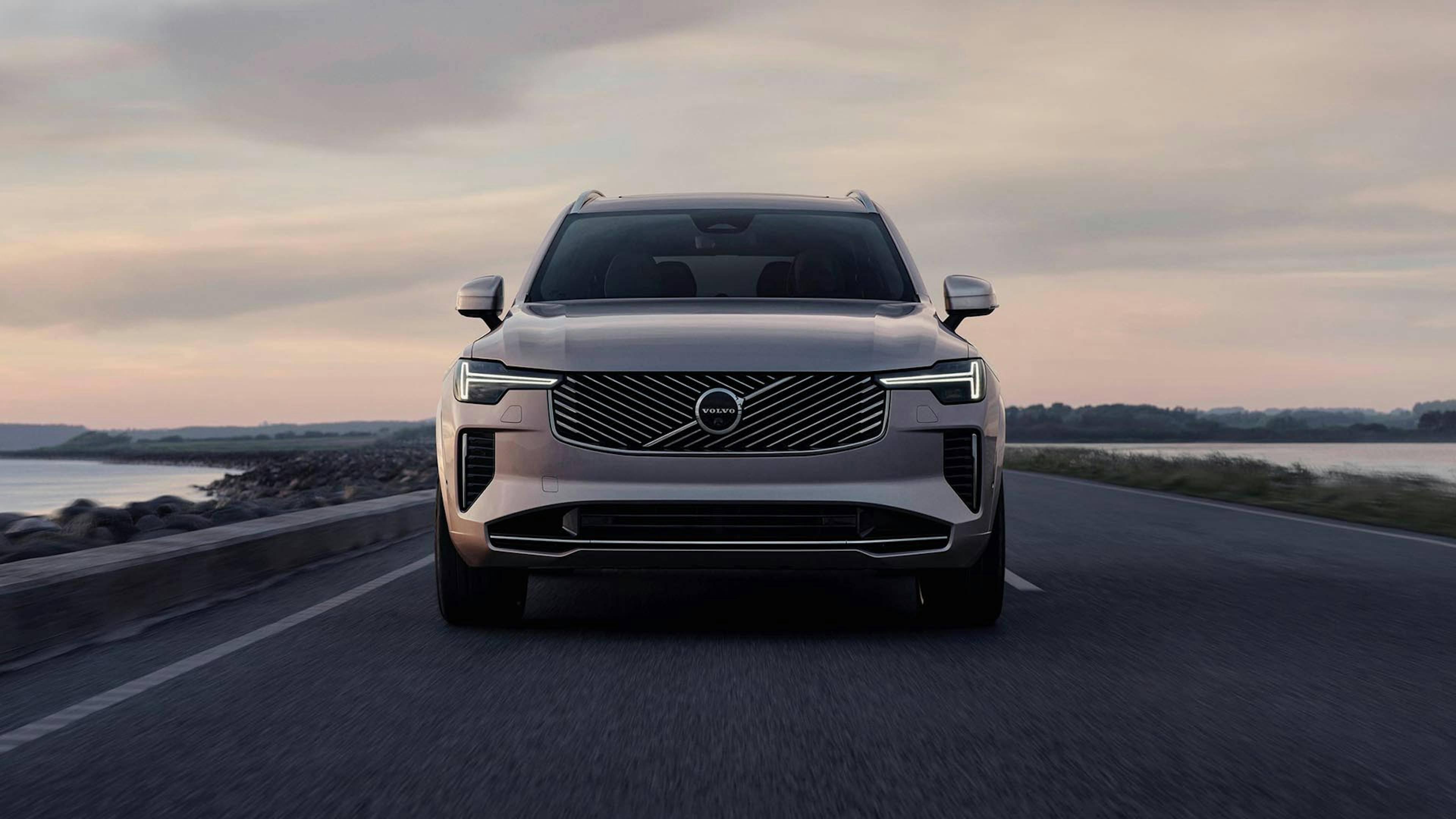 Ein silberner Volvo XC90 fährt über eine Küstenstraße.