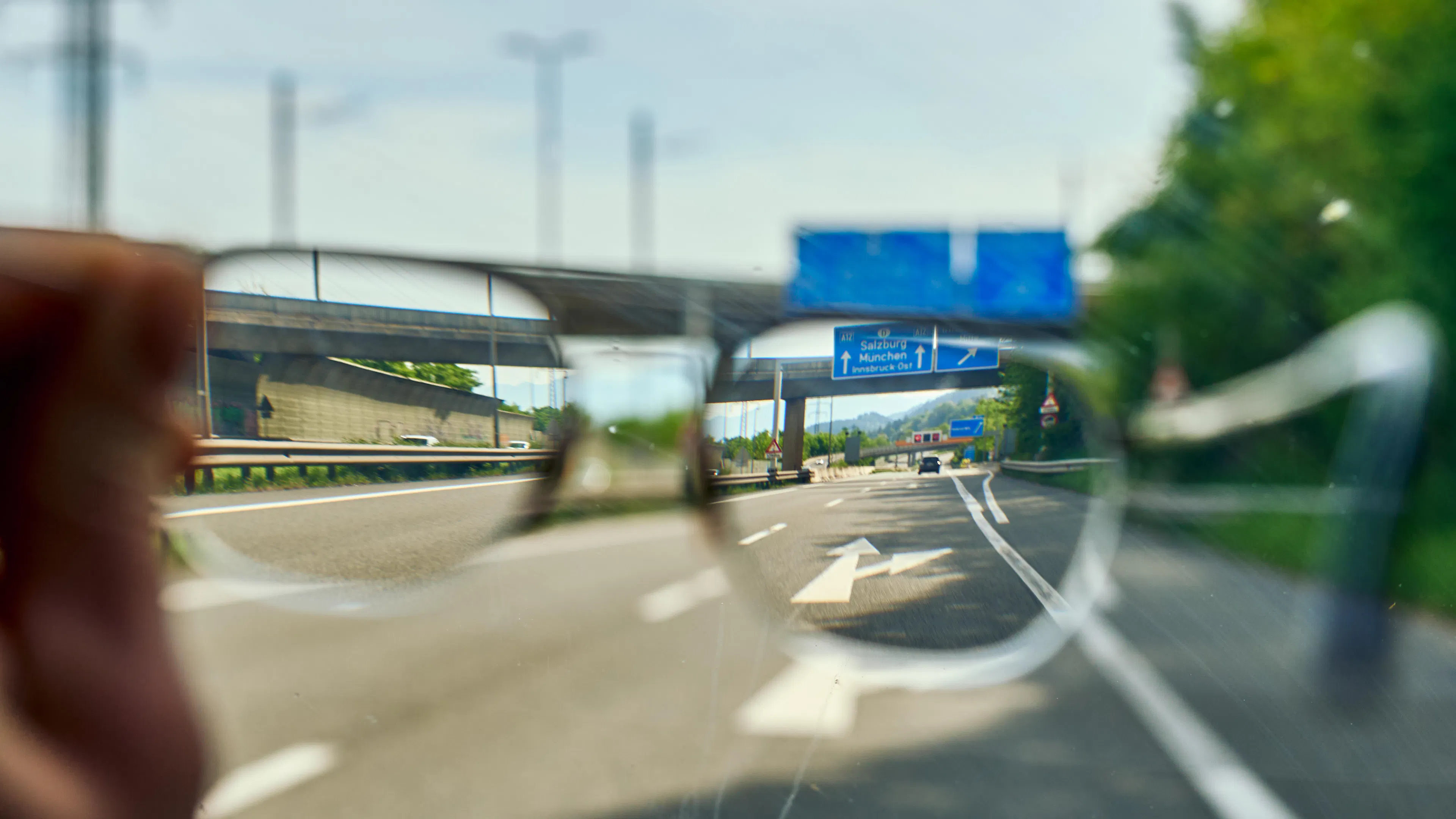 Ein Blick durch eine Brille auf eine Autobahn mit einem blauen Verkehrsschild, das Richtungen nach Salzburg, München und Innsbruck anzeigt, wobei der Bereich außerhalb der Brillengläser unscharf erscheint.