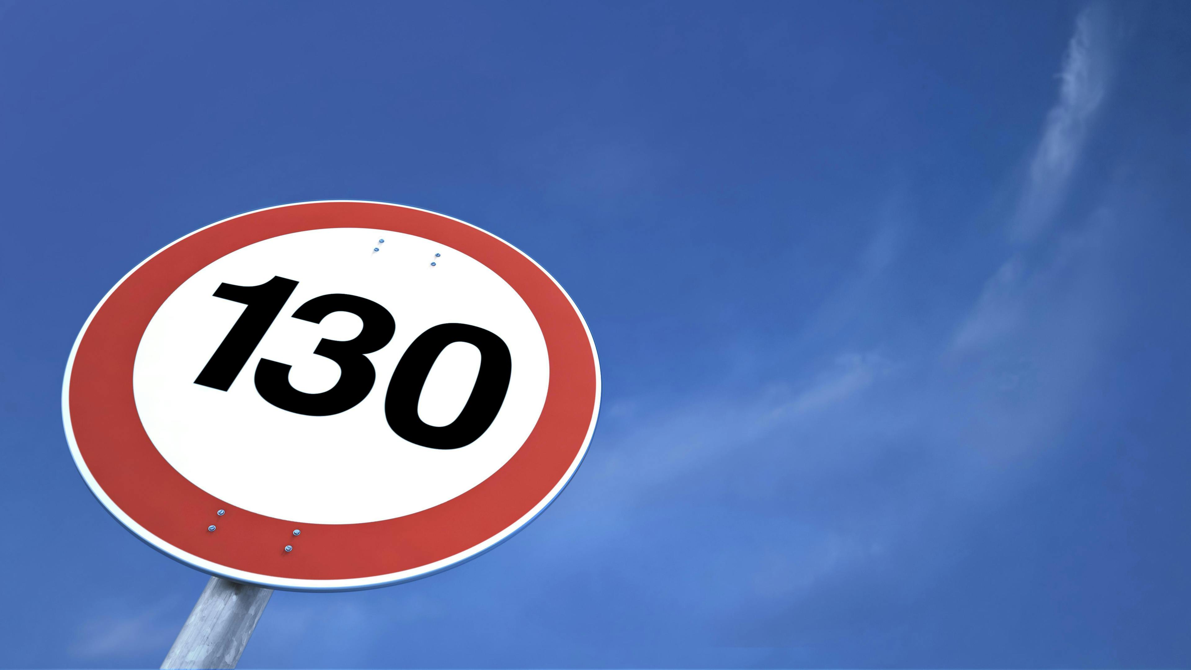 A speed limit sign with the inscription 130 in front of a clear, blue sky. The sign can be seen in close-up, with no visible surroundings or traffic.