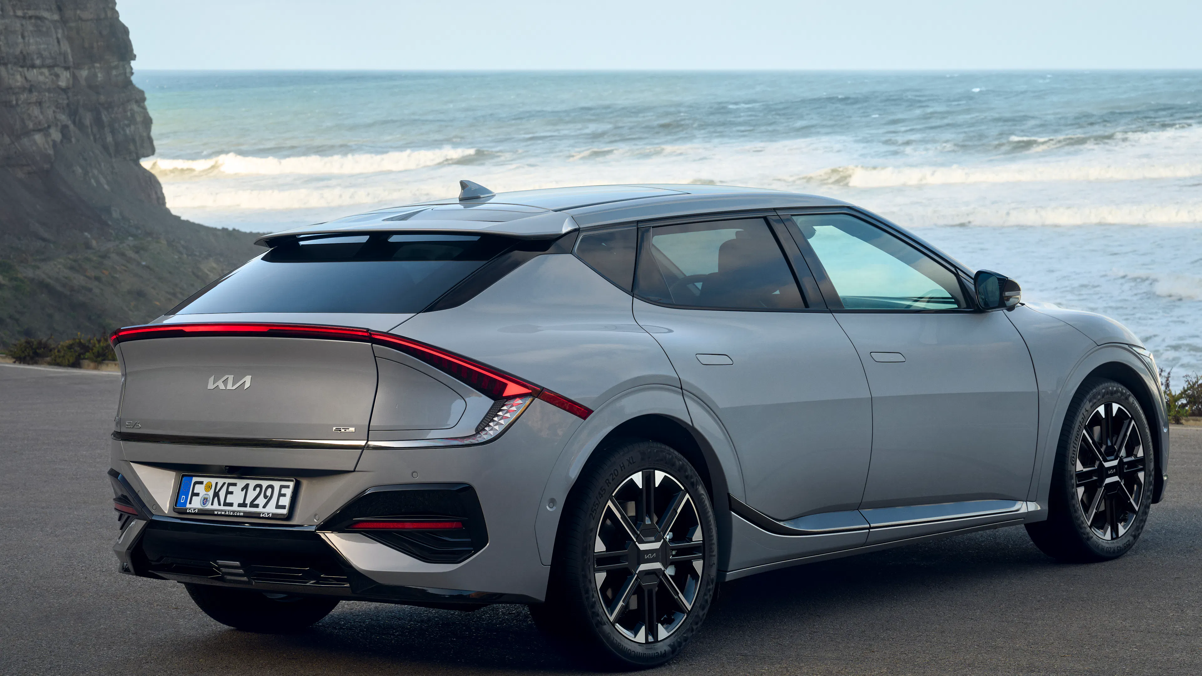 Gray Kia EV6 facelift in the rear view, standing in front of the sea.