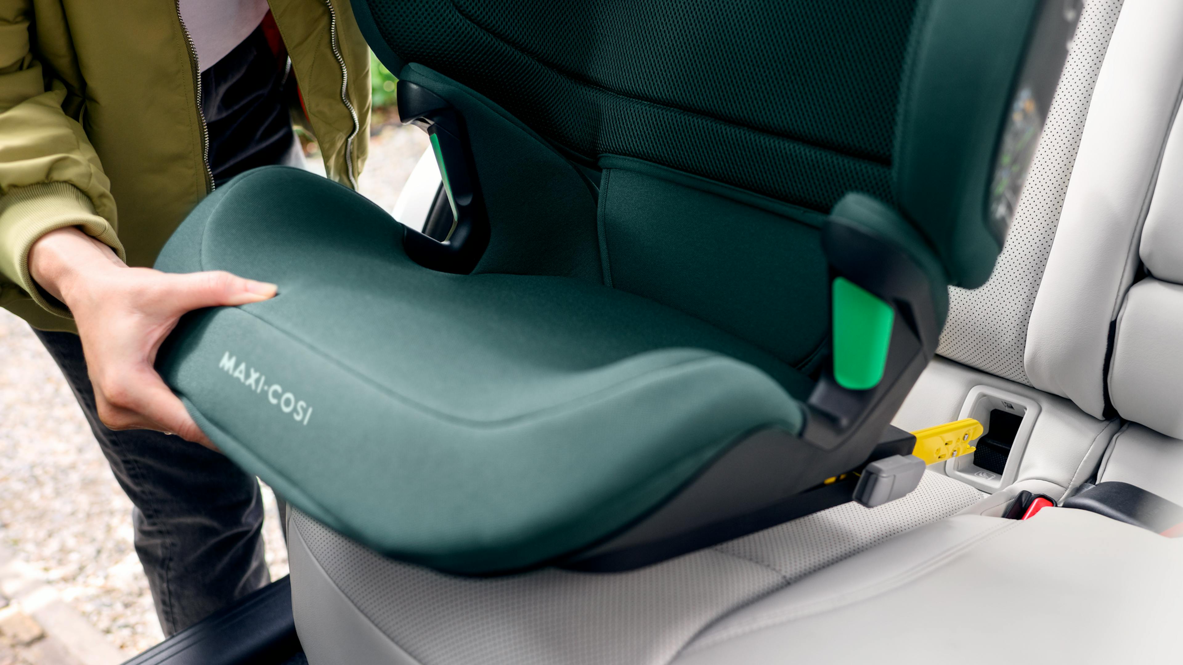 A person installs a Maxi-Cosi child seat with Isofix attachment on the back seat of a car.