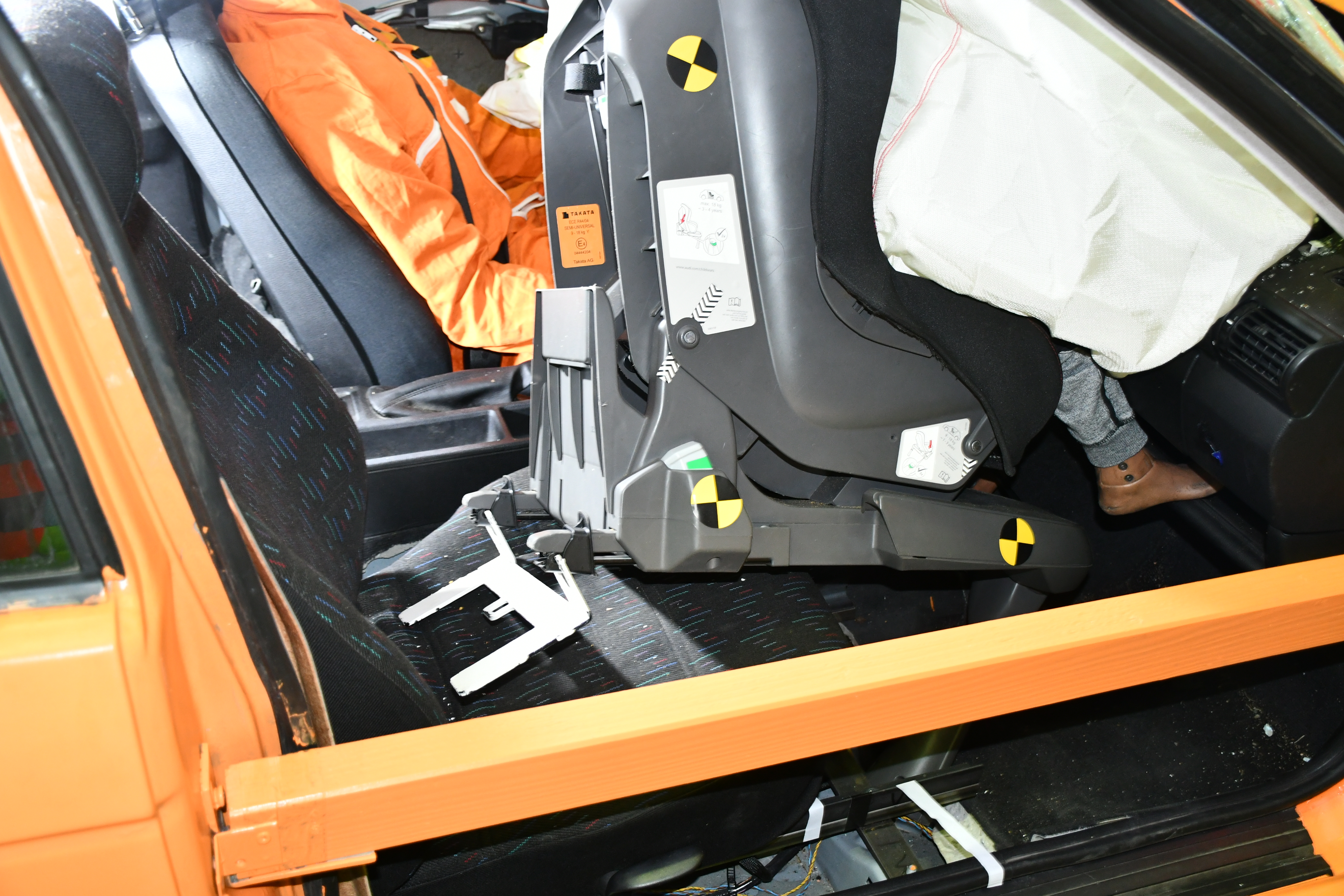 A car seat is tested in a crash test on the passenger side while the airbags are triggered and a dummy sits in the driver's seat.