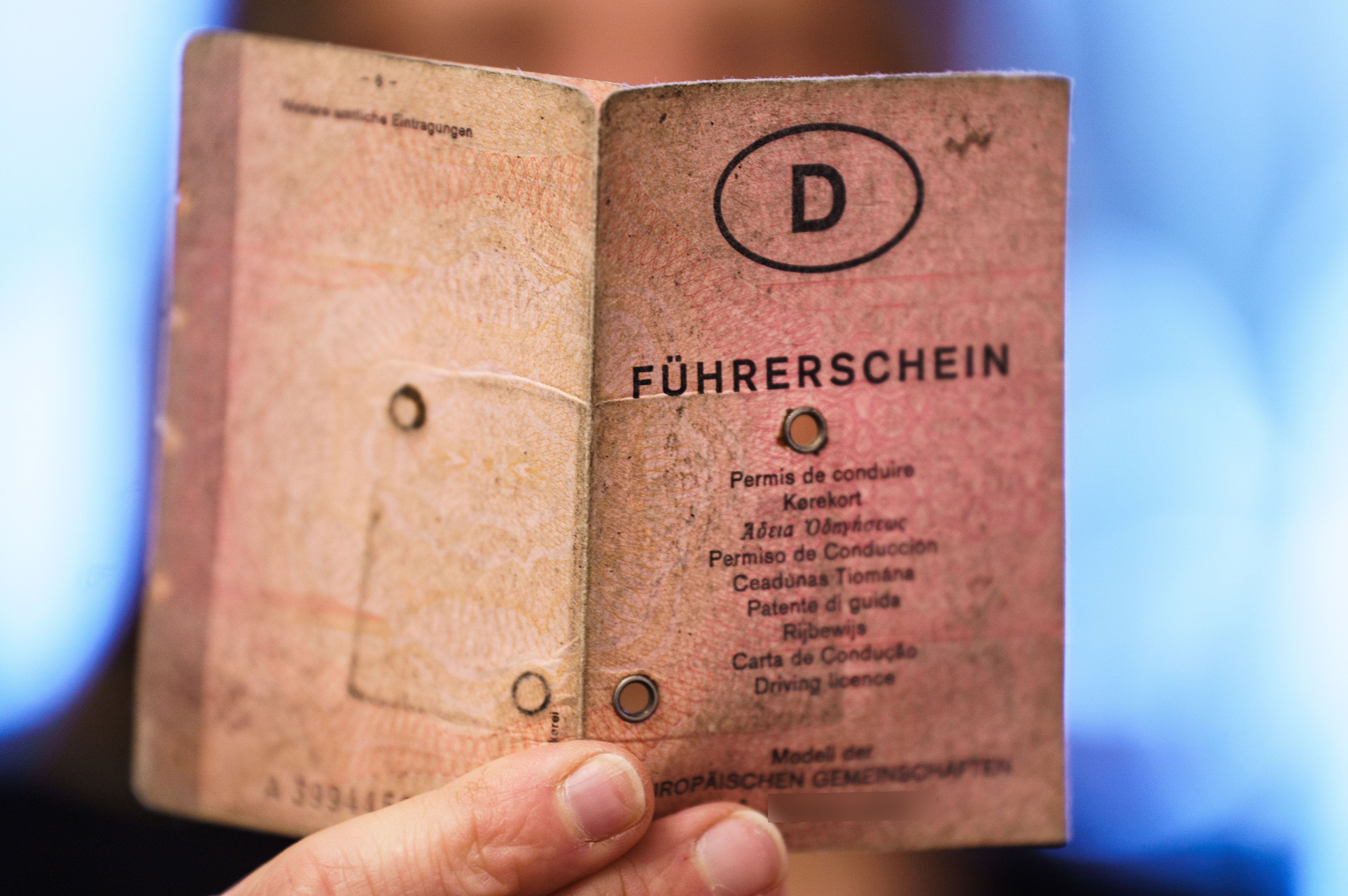 An old, pink German driver's license in paper format is held by one hand, with a capital "D" and the inscription "Führerschein" in different languages on it.
