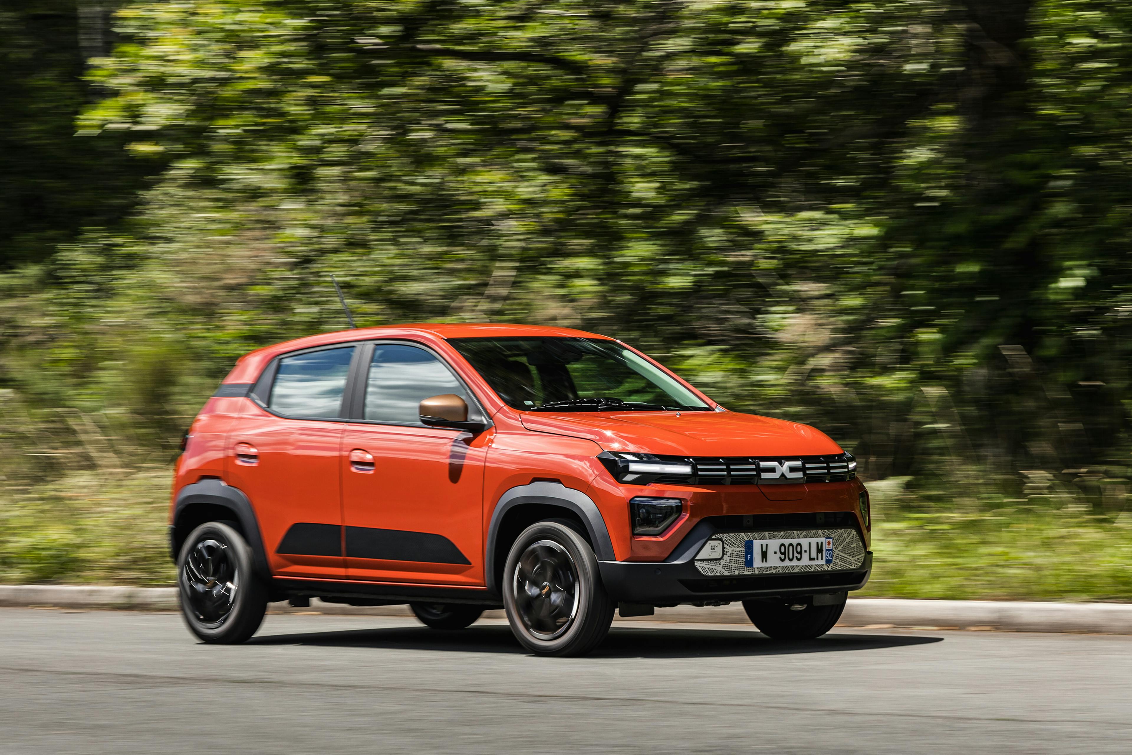 Ein roter Dacia Spring fährt vor grünem Hintergrund von links nach rechts durch das Bild.