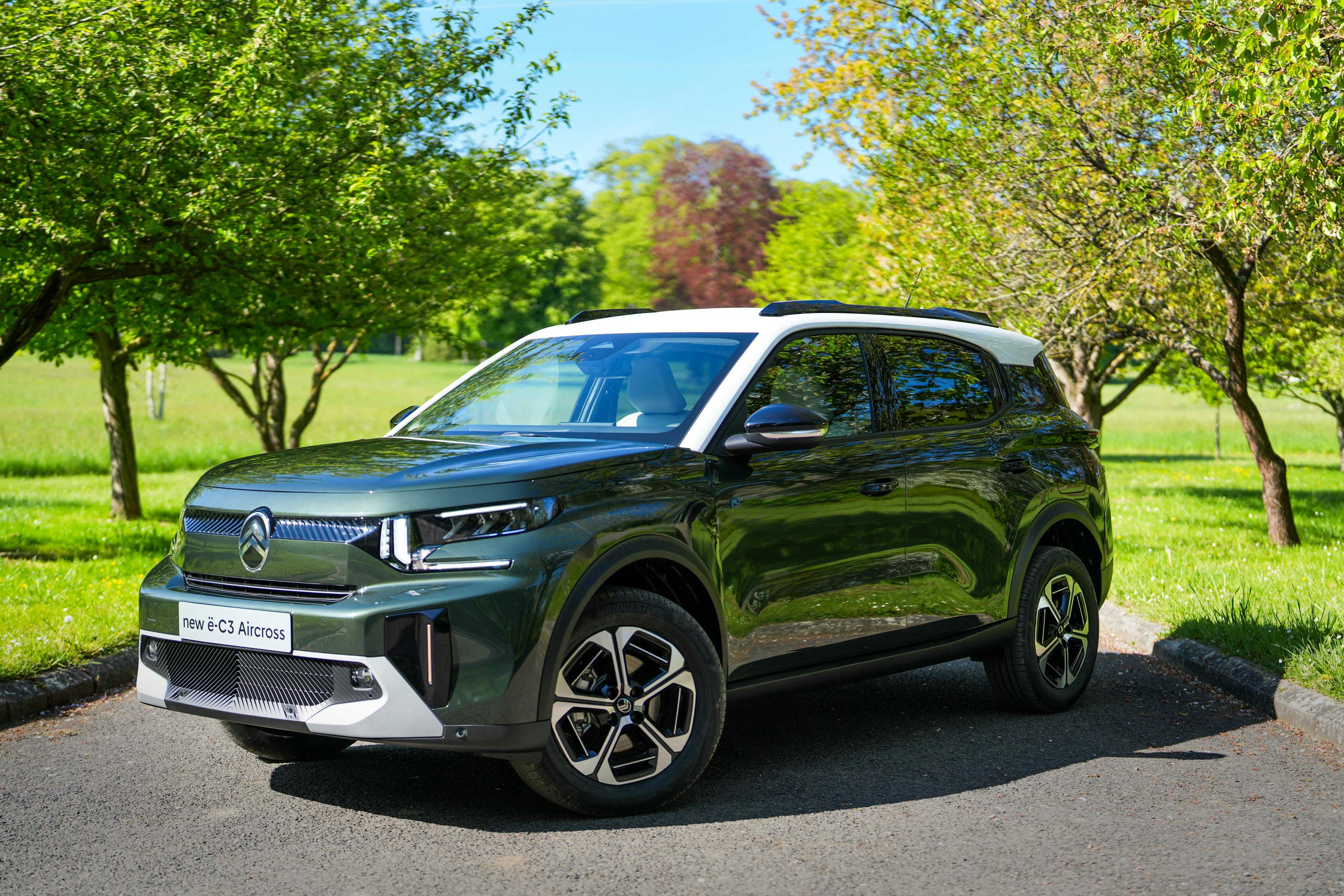 Ein grüner Citroën ë-C3 Aircross steht auf einer Straße zwischen Bäumen.