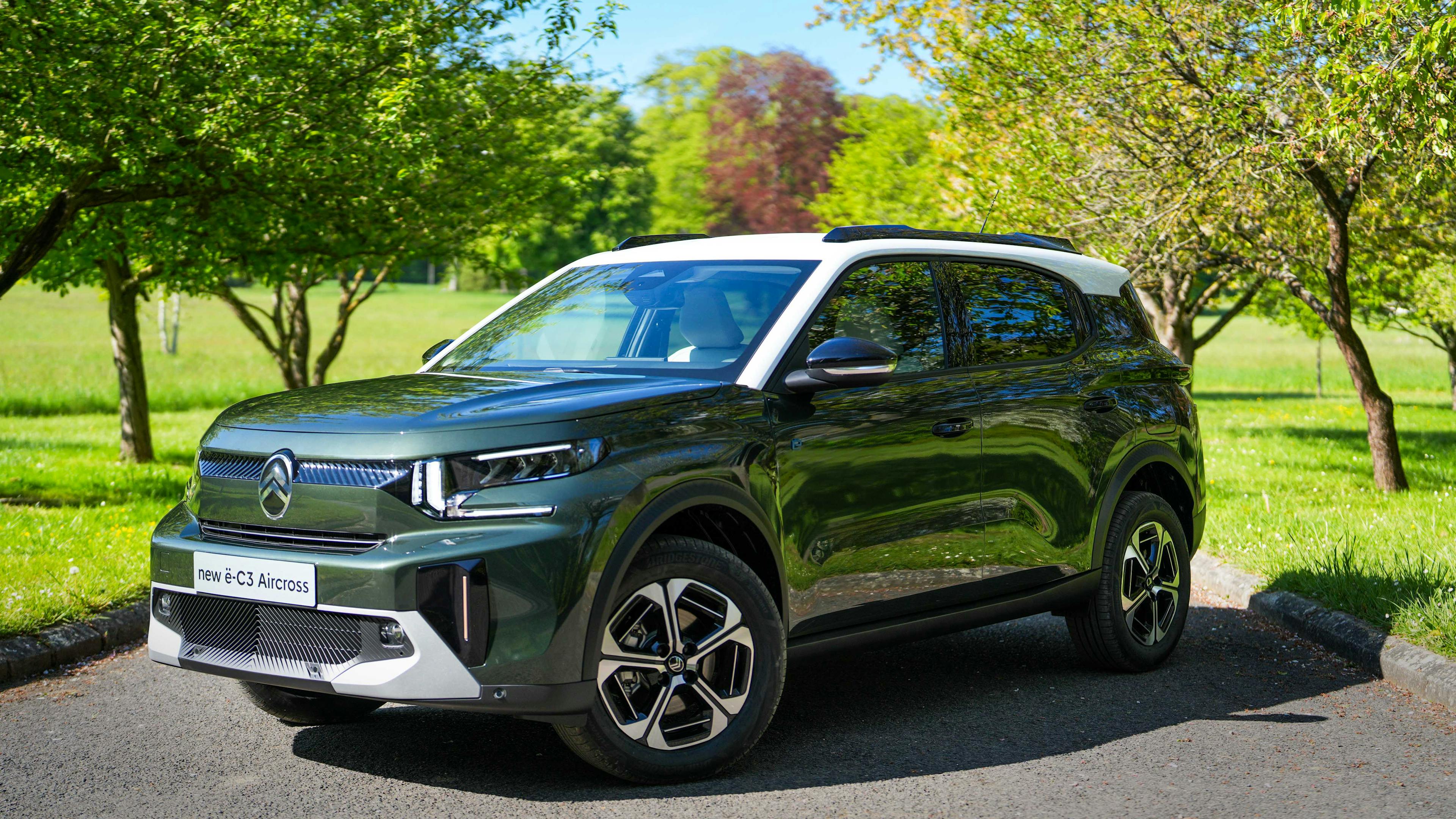 A green Citroën ë-C3 Aircross is parked on a road between trees.