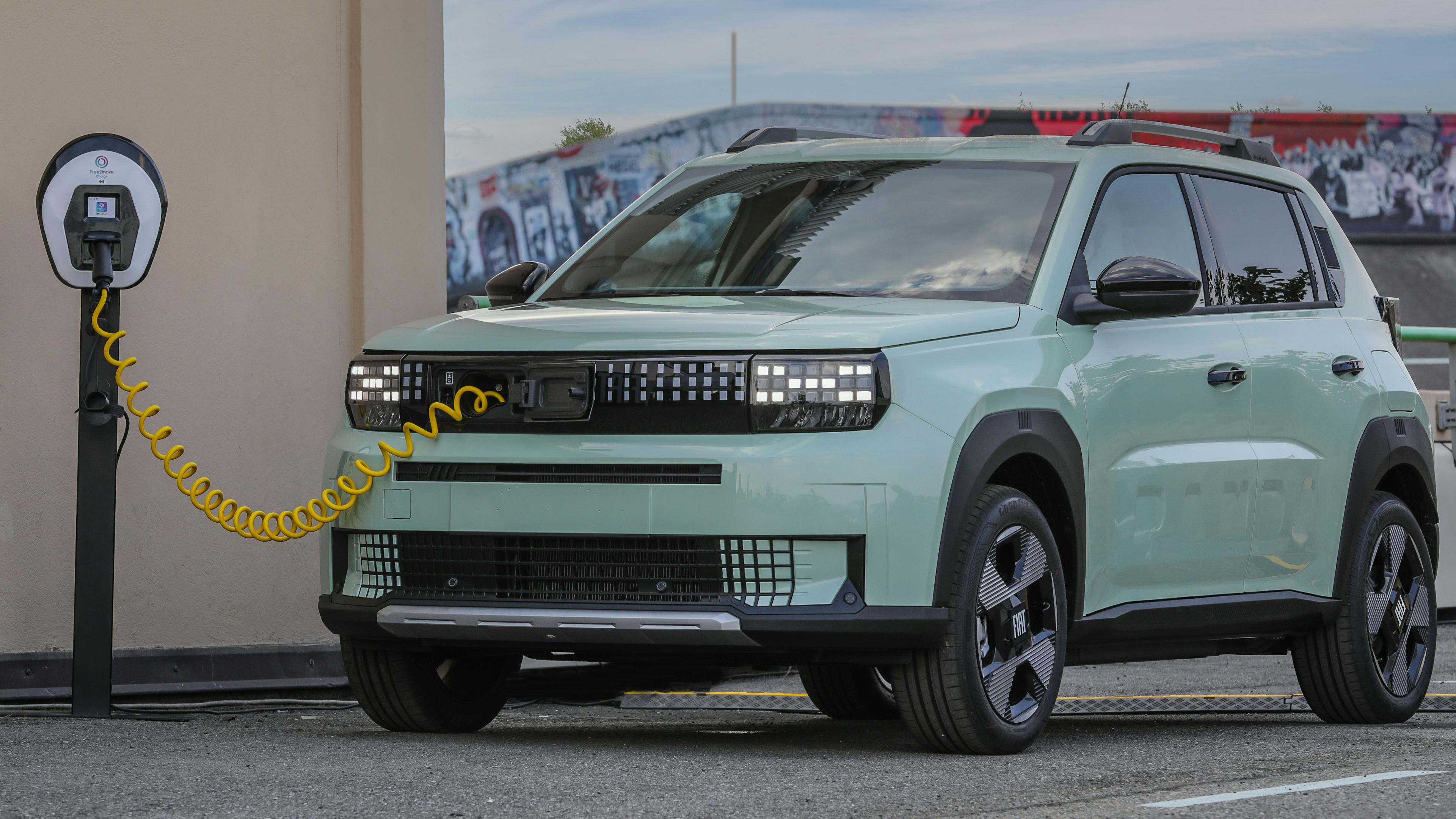A mint green Fiat Grande Panda stands at a charging station.