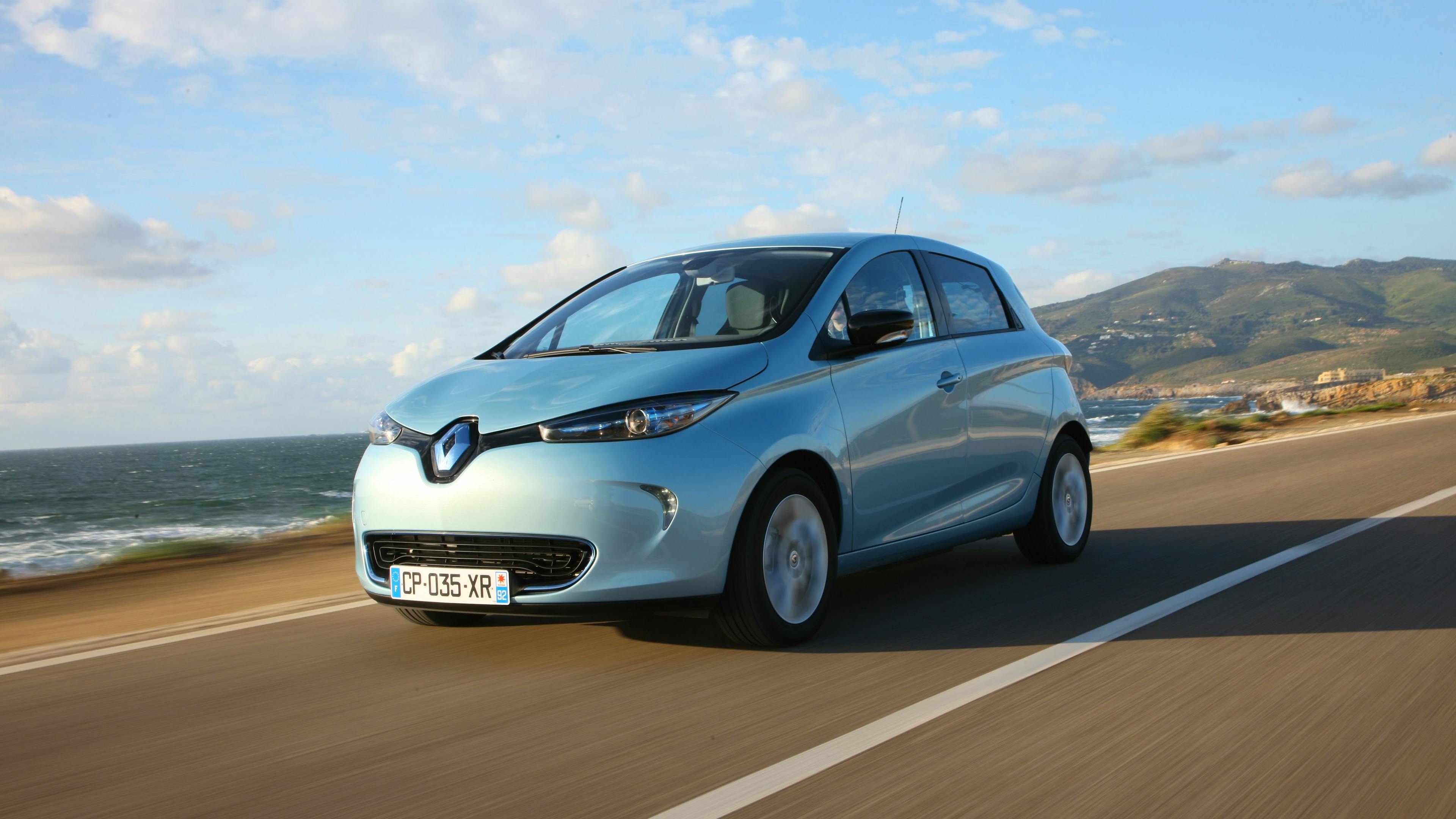 A silver Renault Zoe is driving along a coastal road.