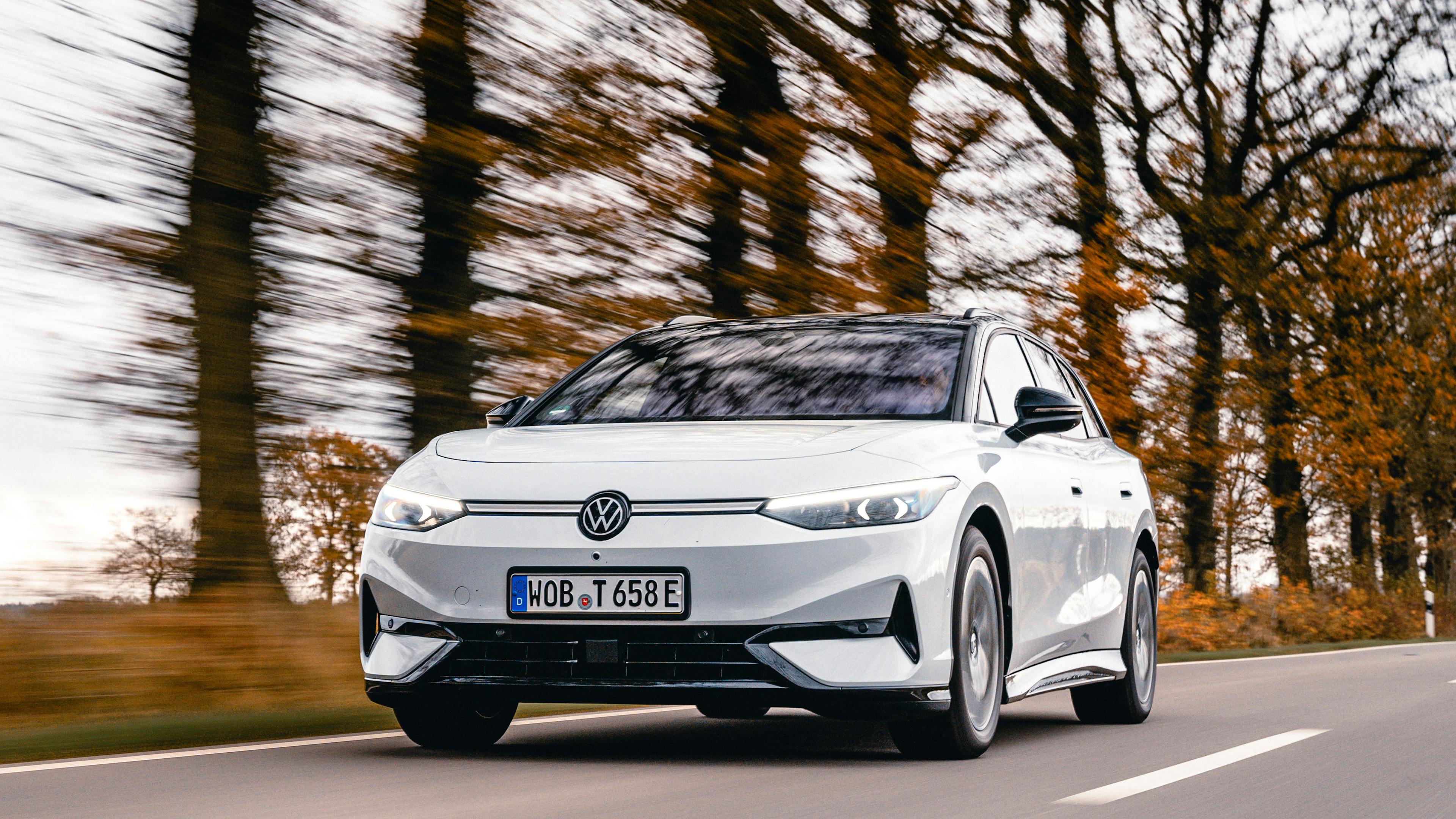 A white VW ID.7 Tourer is driving on a country road with trees in the background.