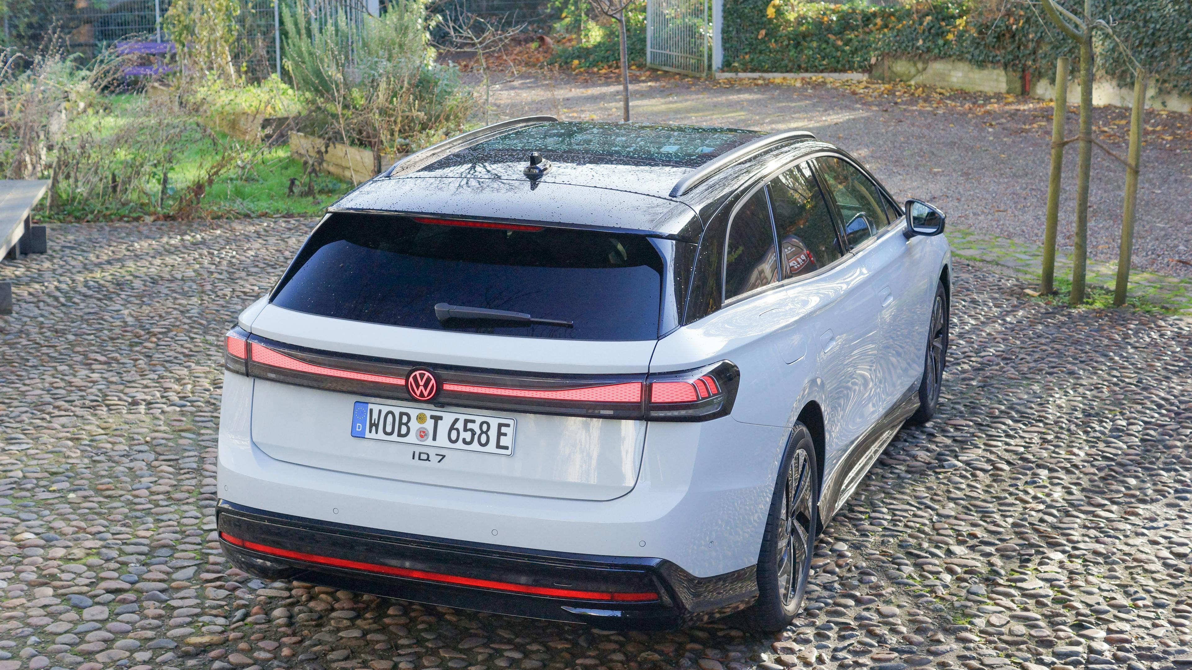 Rear view of a white VW ID.7 Tourer with the taillight on, parked on cobblestones.